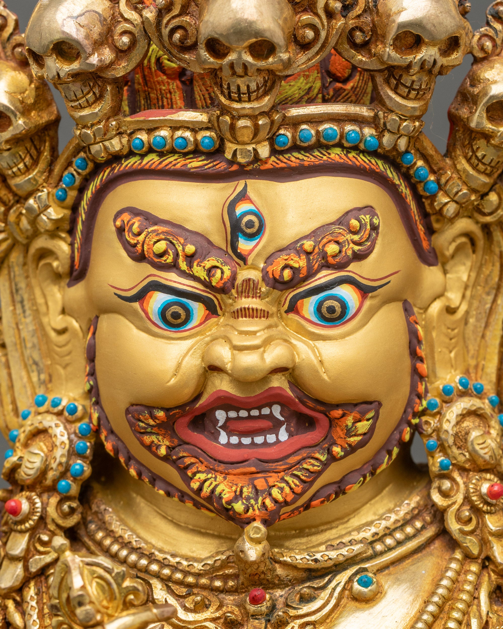 Gold-painted wrathful face of Mahakala with five-skull diadem, Tibetan protector deity.