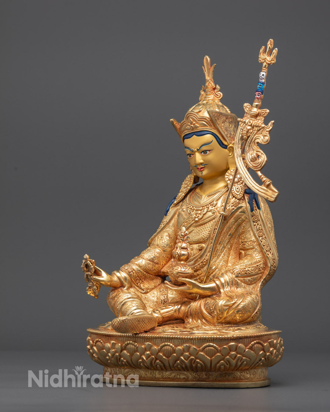 Guru Padmasambhava statue holding 9-pronged vajra, skull cup with vase, and trident (khatvanga) – symbols of tantric power and spiritual transformation.