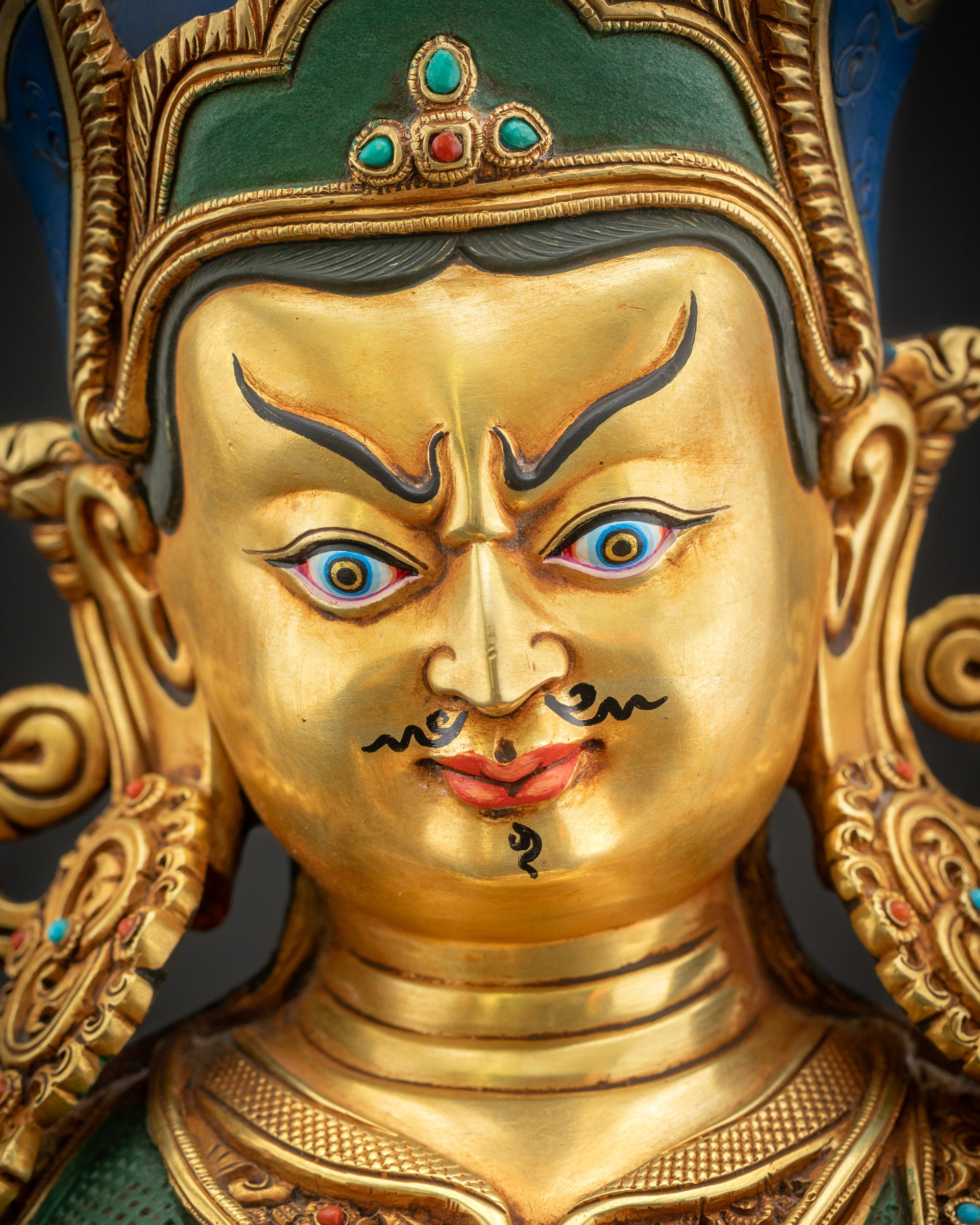 Detailed close-up of Guru Rinpoche face, hand-carved copper with gold fire-gilded highlights.