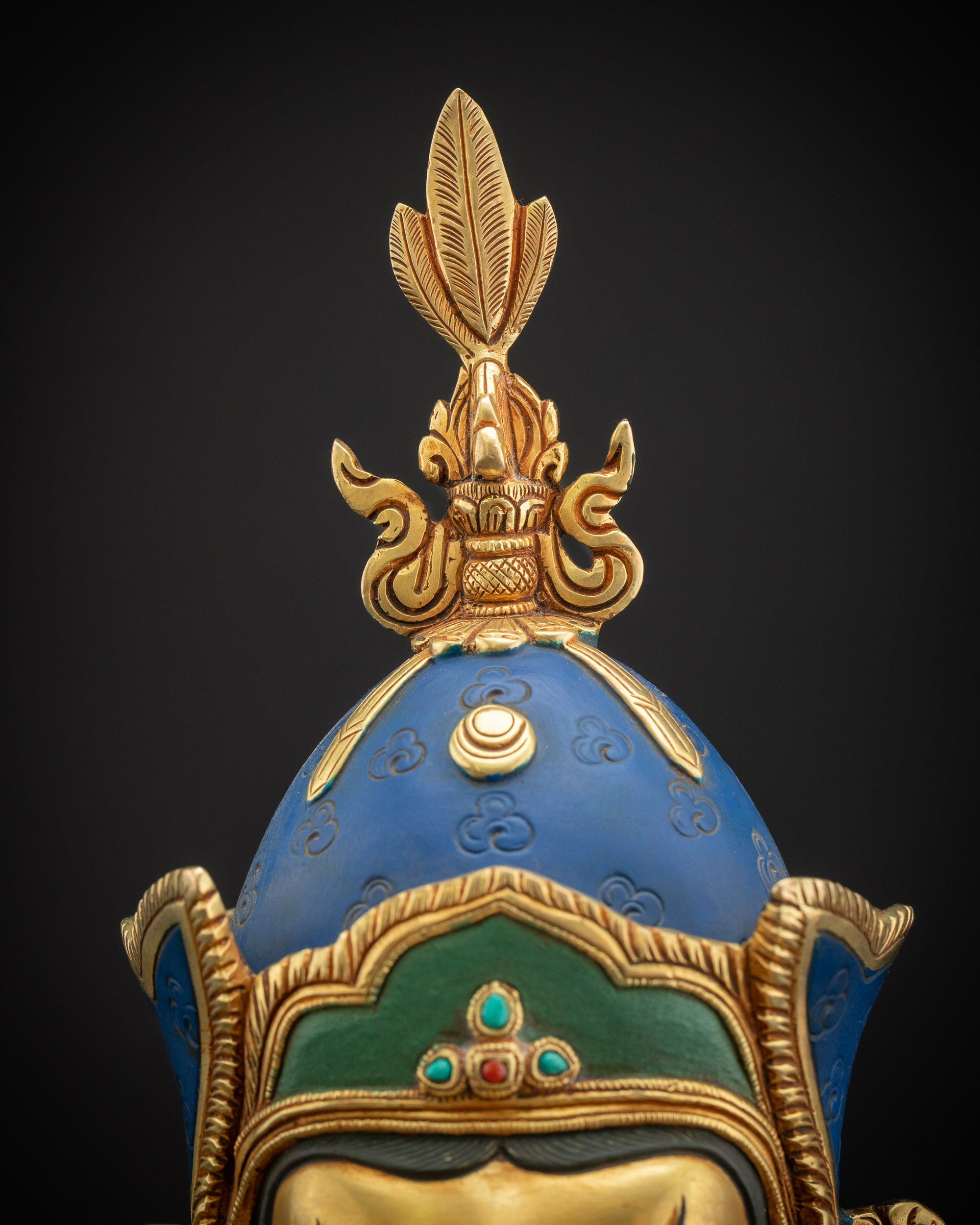 Close-up of Guru Rinpoche lotus hat with vulture feather finial, detailed gold and copper work.