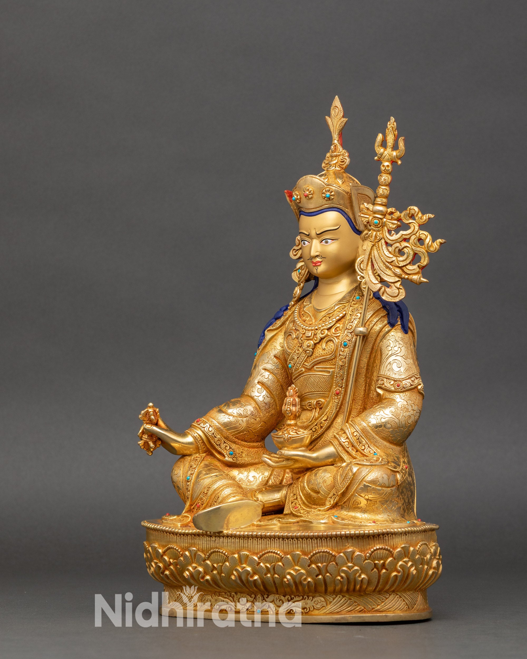 Left profile of Guru Rinpoche statue with intricate lotus throne and sacred Vajrayana attributes