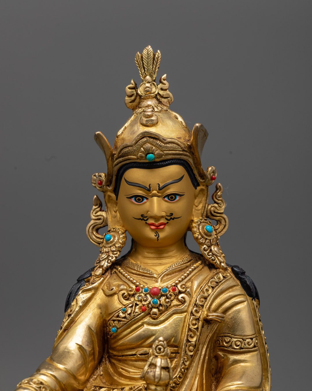 Padmasambhava statue adorned with semi-precious stones, crowned with eagle feather and jewel-ornamented earrings, offering divine protection for sacred spaces.