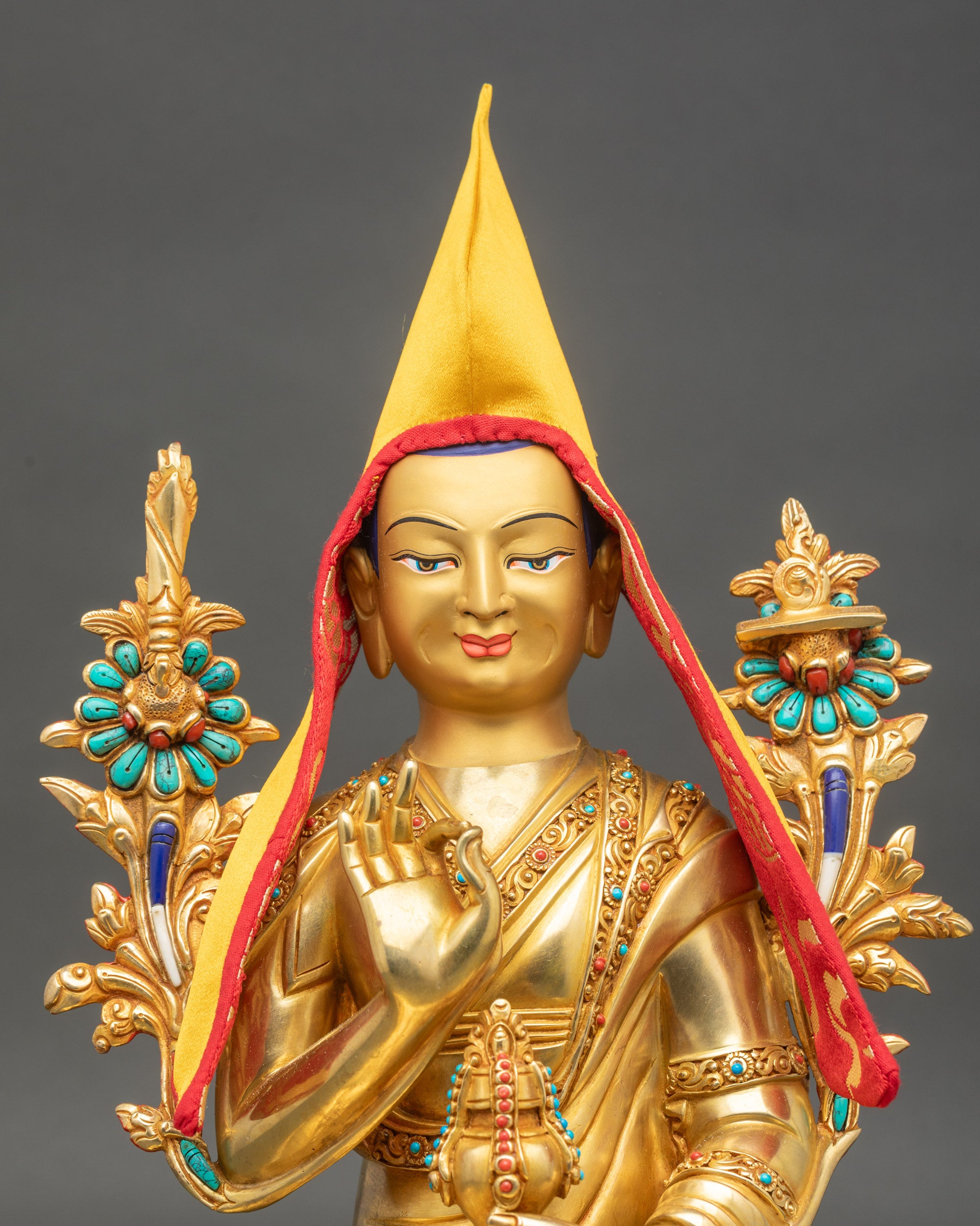 Regular close-up of Je Tsongkhapa statue showing serene gold-painted face and red pandita hat with brocade trim