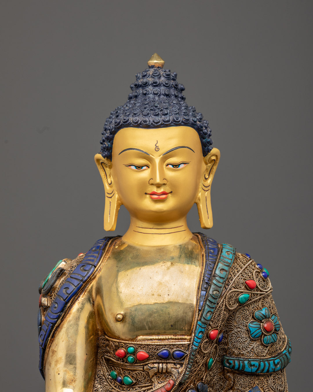 Shakyamuni Buddha’s serene gold-gilded face and intricately detailed Kasaya robe with turquoise, coral, and lapis lazuli accents