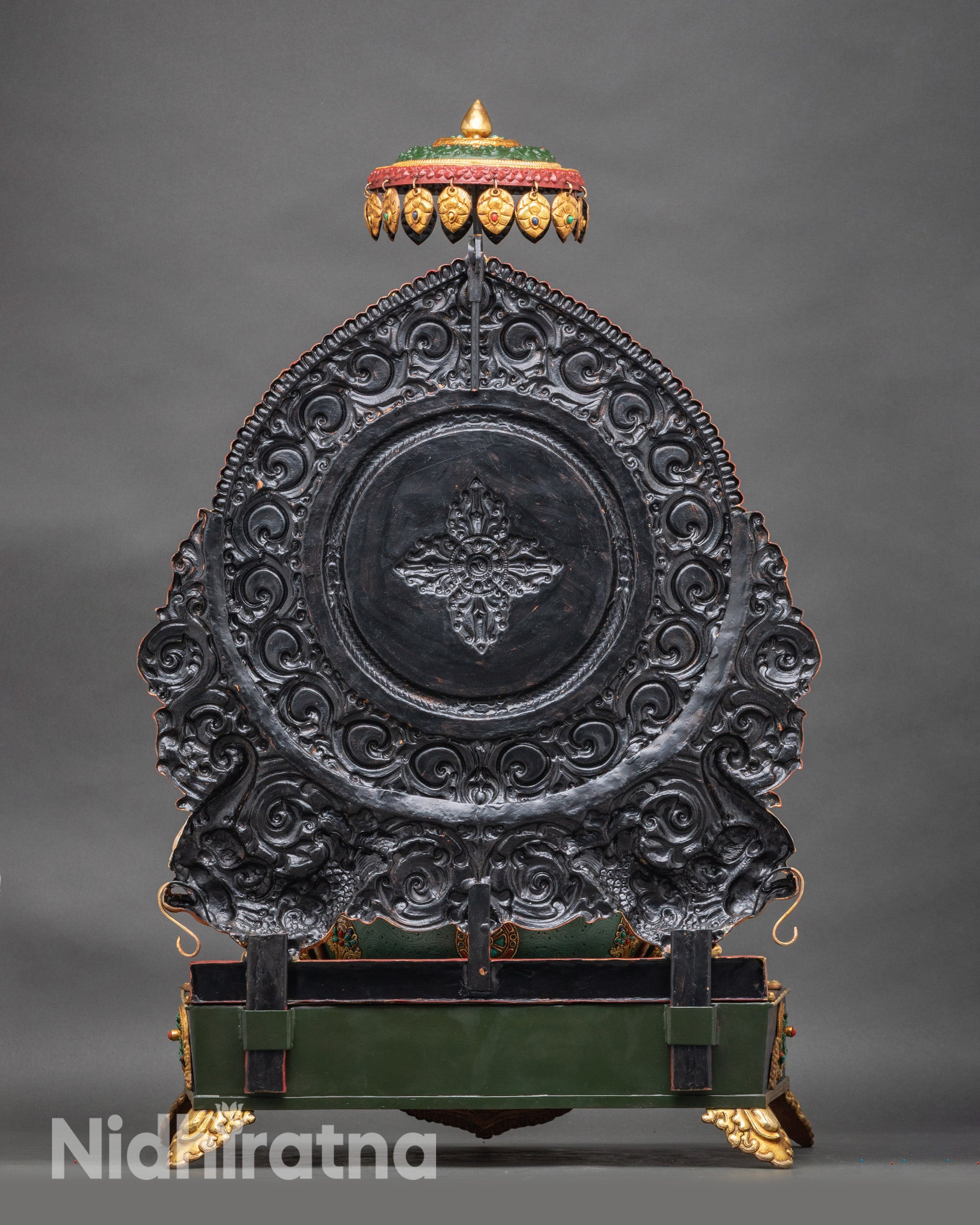 Shakyamuni Buddha statue viewed from back showing ornate throne backdrop with green halo and cloud motif scrollwork