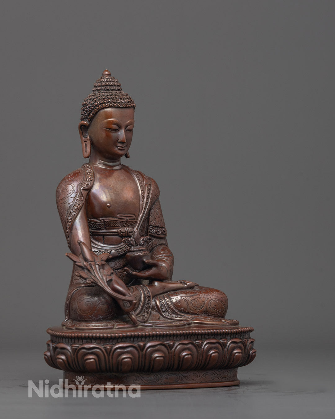Side angle of hand-carved oxidized copper Medicine Buddha with monk’s robe details