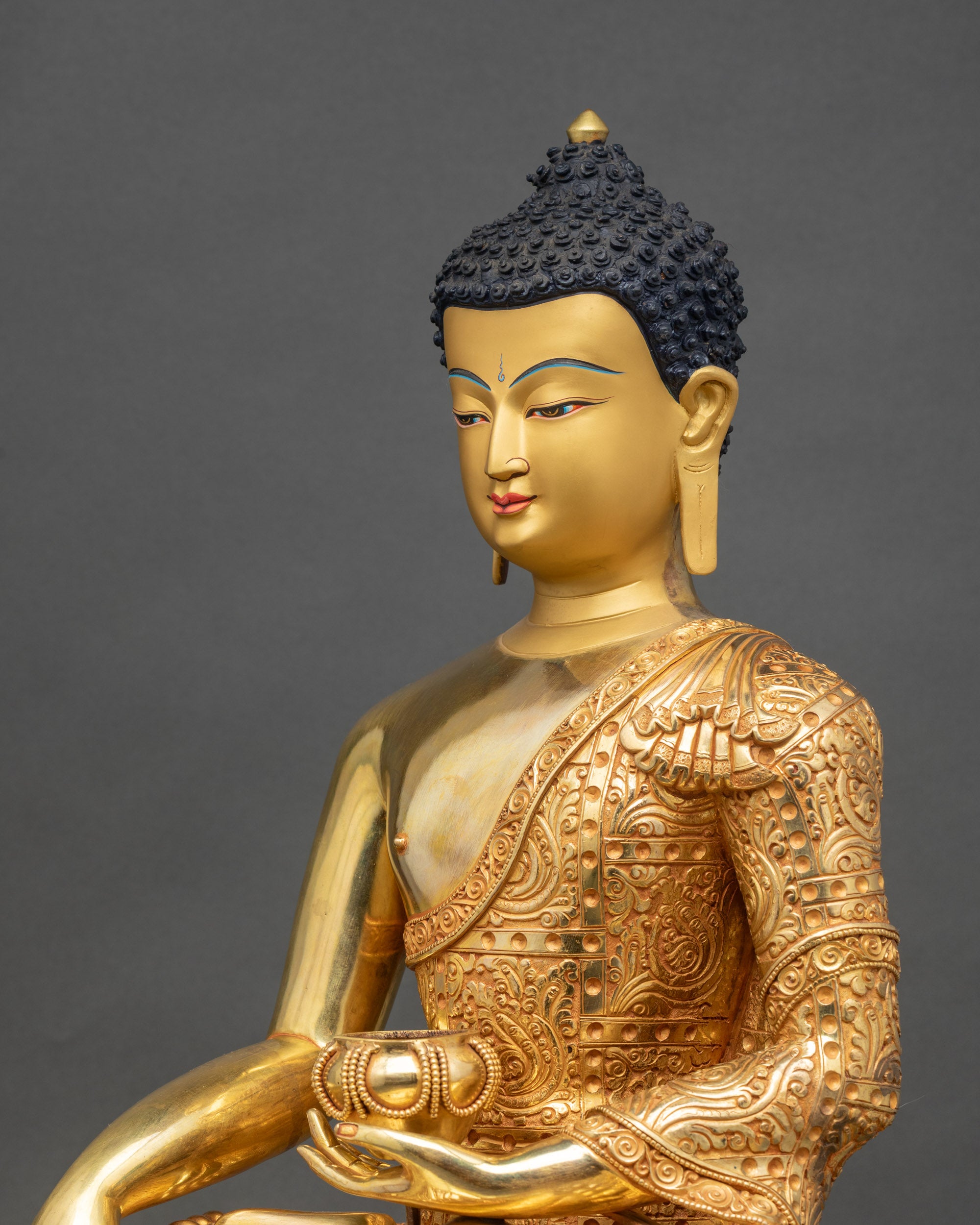 Side close-up of Buddha statue, carved monastic robe and delicate floral gold motifs visible