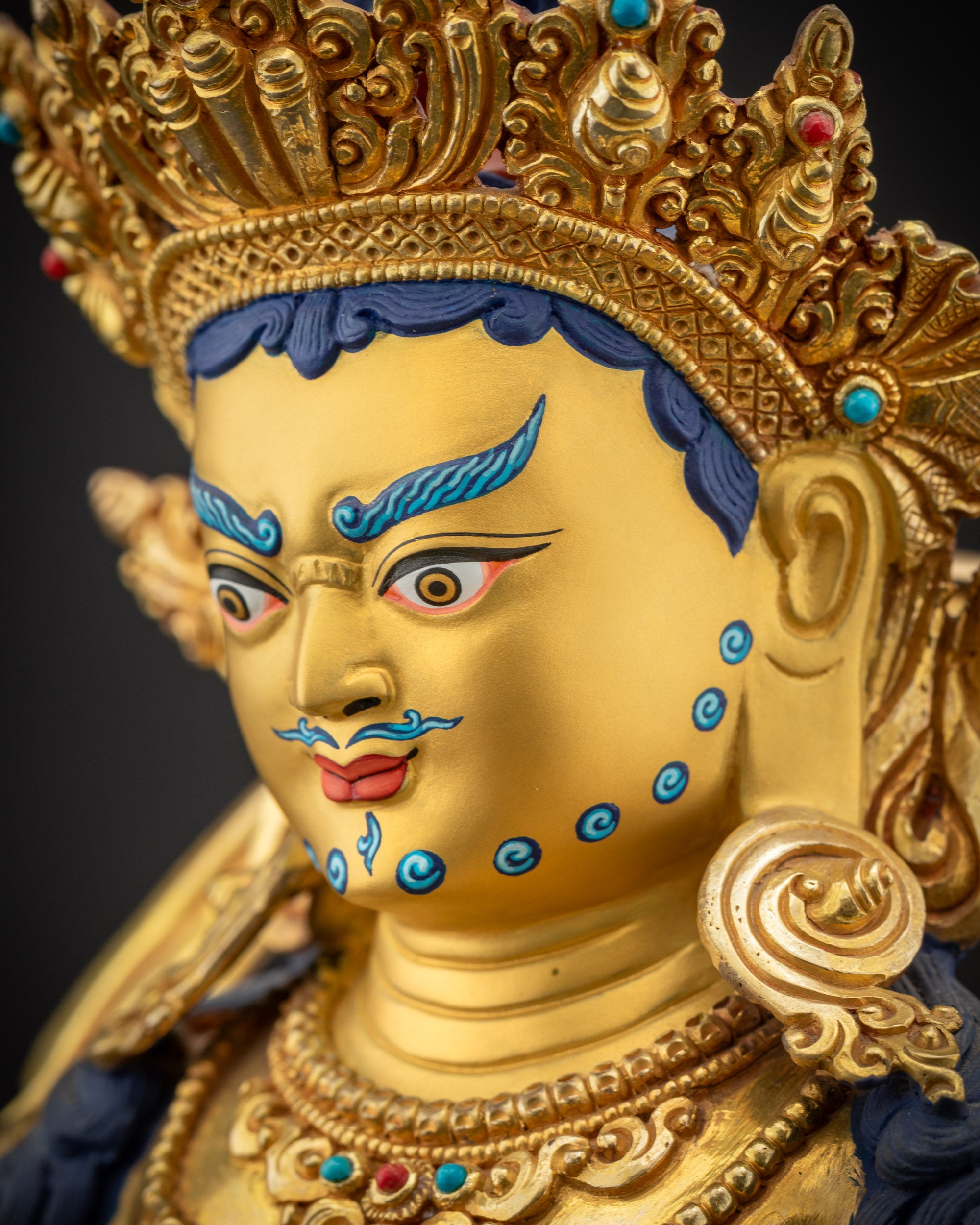 Side close up face Dzambhala statue showing five-shell crown and elaborate earrings