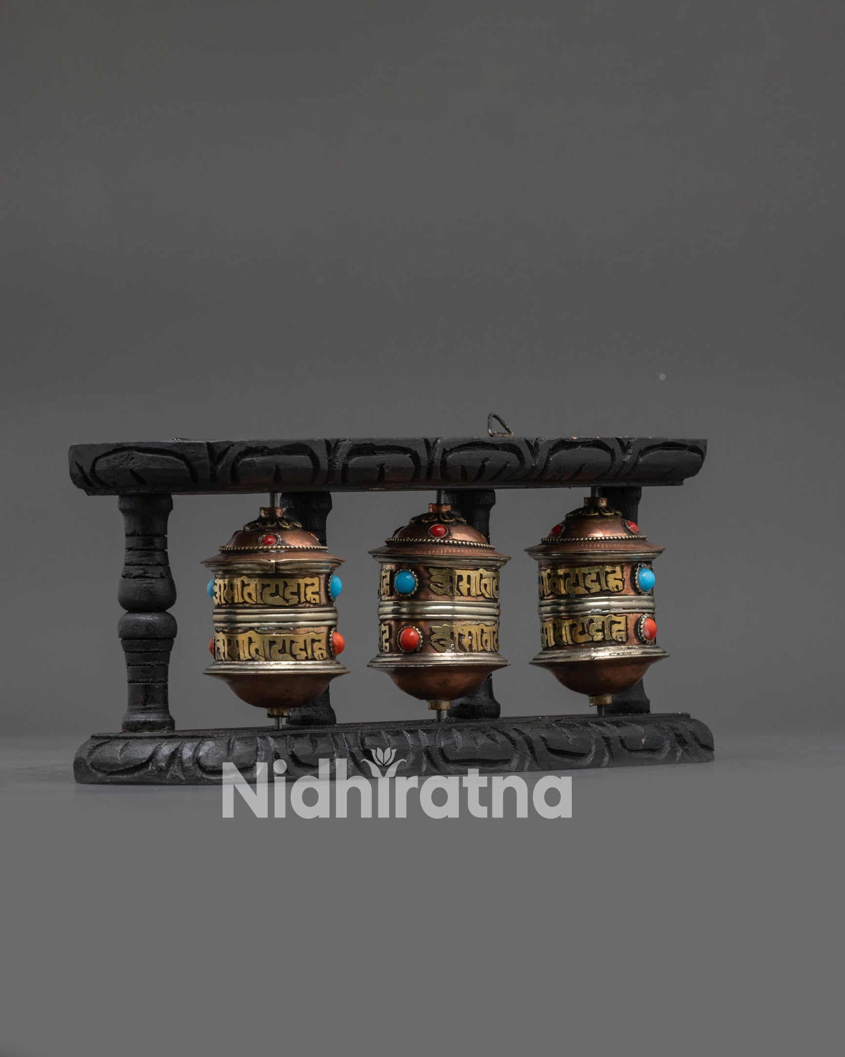 Side view Tibetan prayer wheel set showing carved dark wood frame and brass detailing