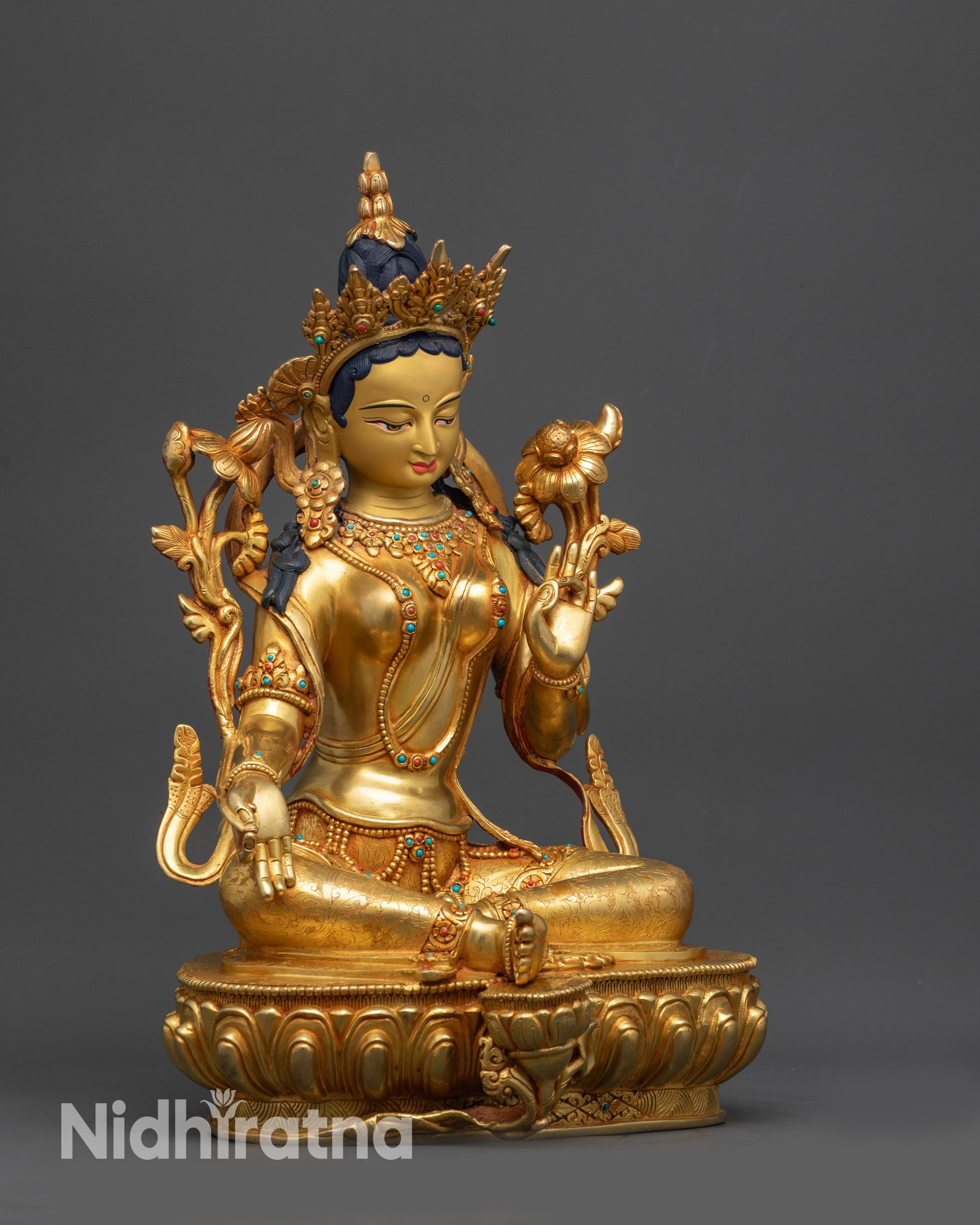 Side view of Green Tara sculpture with varada mudra and blue lotus in hand