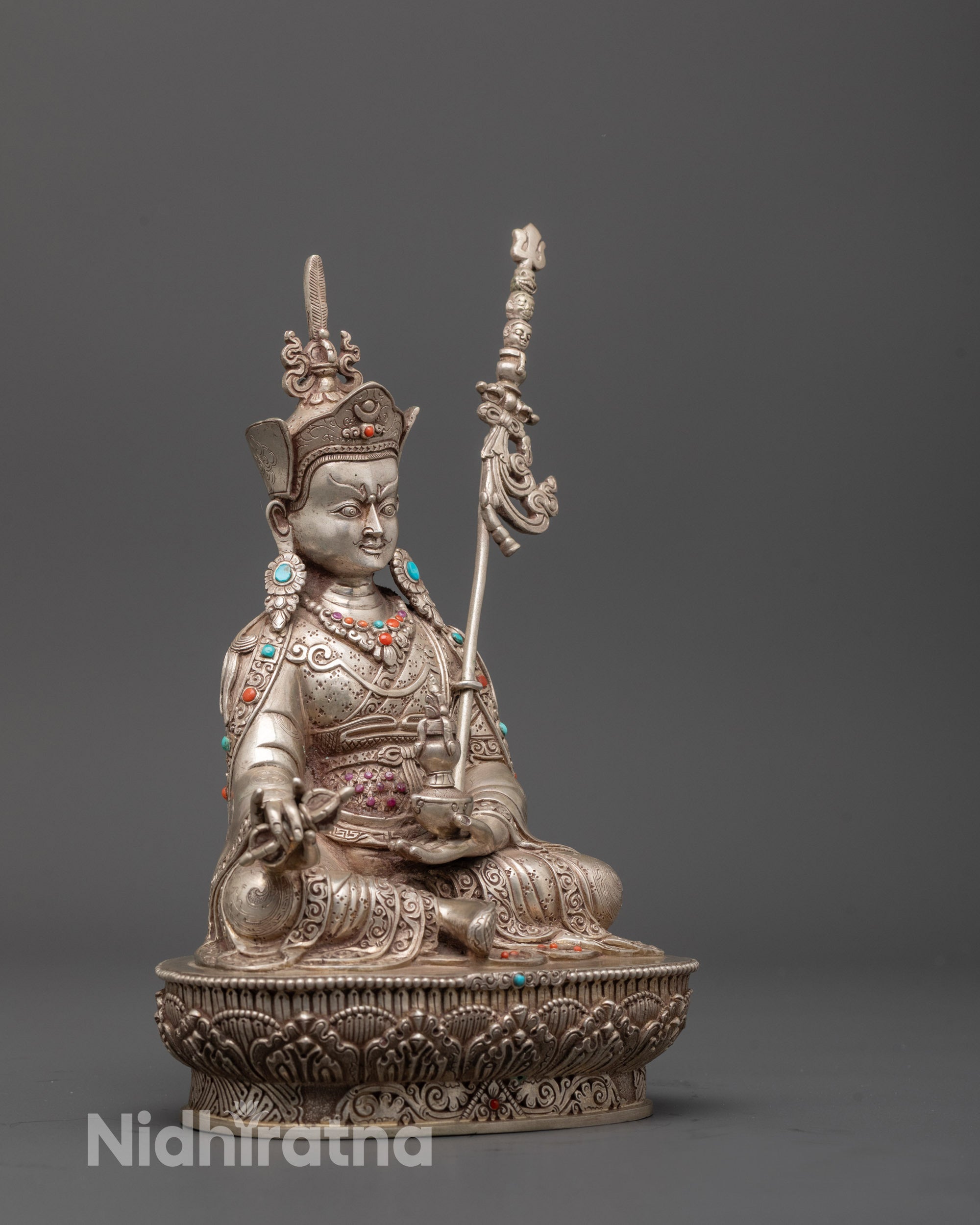 Side view of Guru Rinpoche statue holding vajra, khatvanga, and kapala on lotus seat