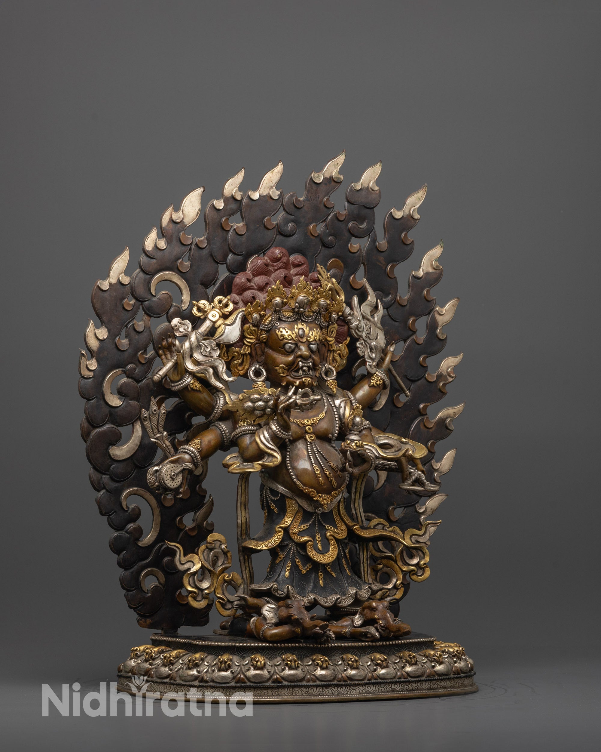 Side view of White Mahakala statue crushing two spirits with flowing robes and jewelry