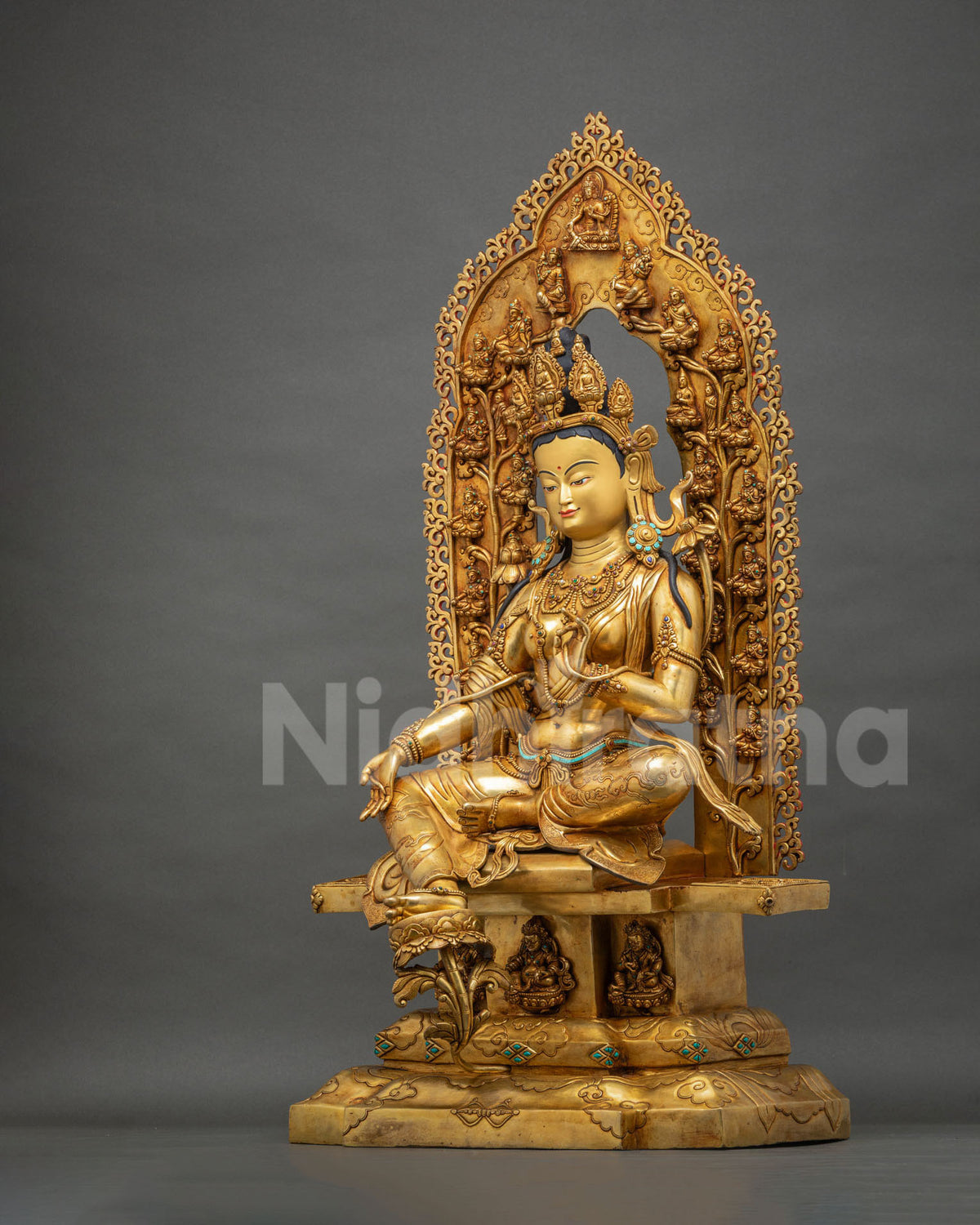 Angled view of Green Tara statue in royal ease with extended right leg and gold fire gilding