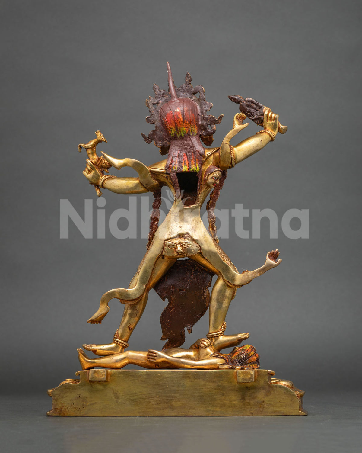 Back view of gold copper Ekajati statue with raised arms and braided hair