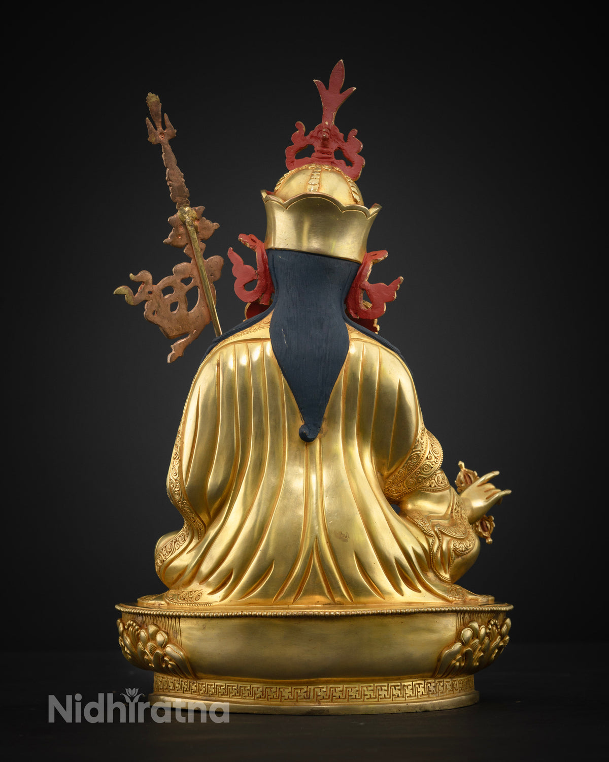 Back view of gold Guru Rinpoche statue showing draped robes, red crown ornaments, and staff