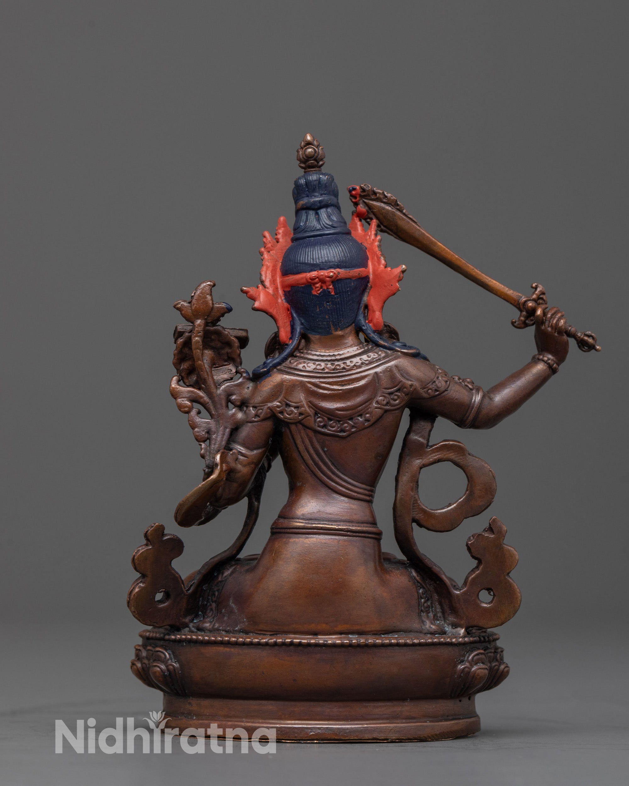 back view of oxidized copper manjushri statue seated gracefully on lotus seat