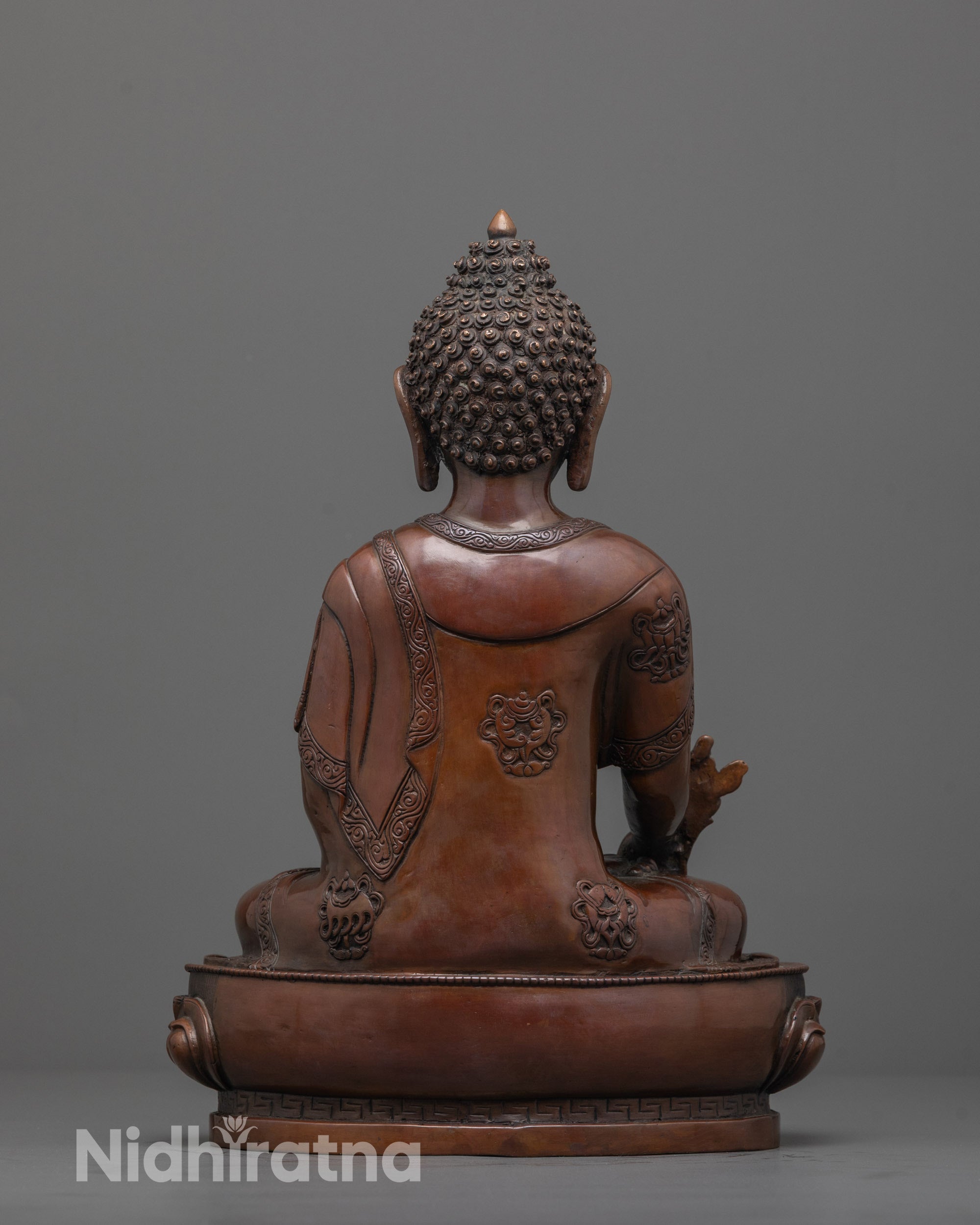 back view of oxidized medicine buddha statue with detailed robe and sacred copper patina