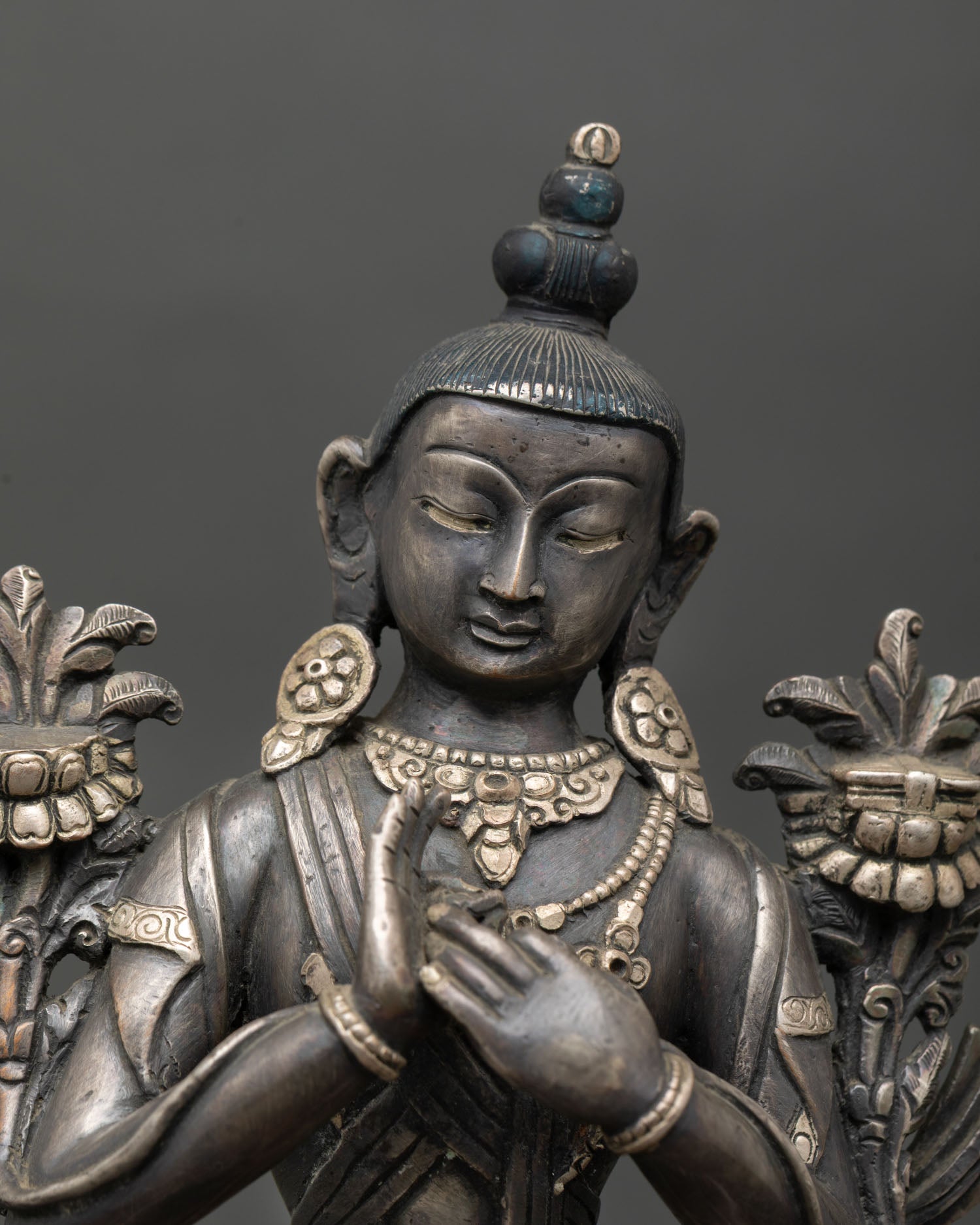 Close up detail of Avalokiteshvara face and dharmachakra mudra showing serene meditative expression silver ornaments and traditional Newari craftsmanship