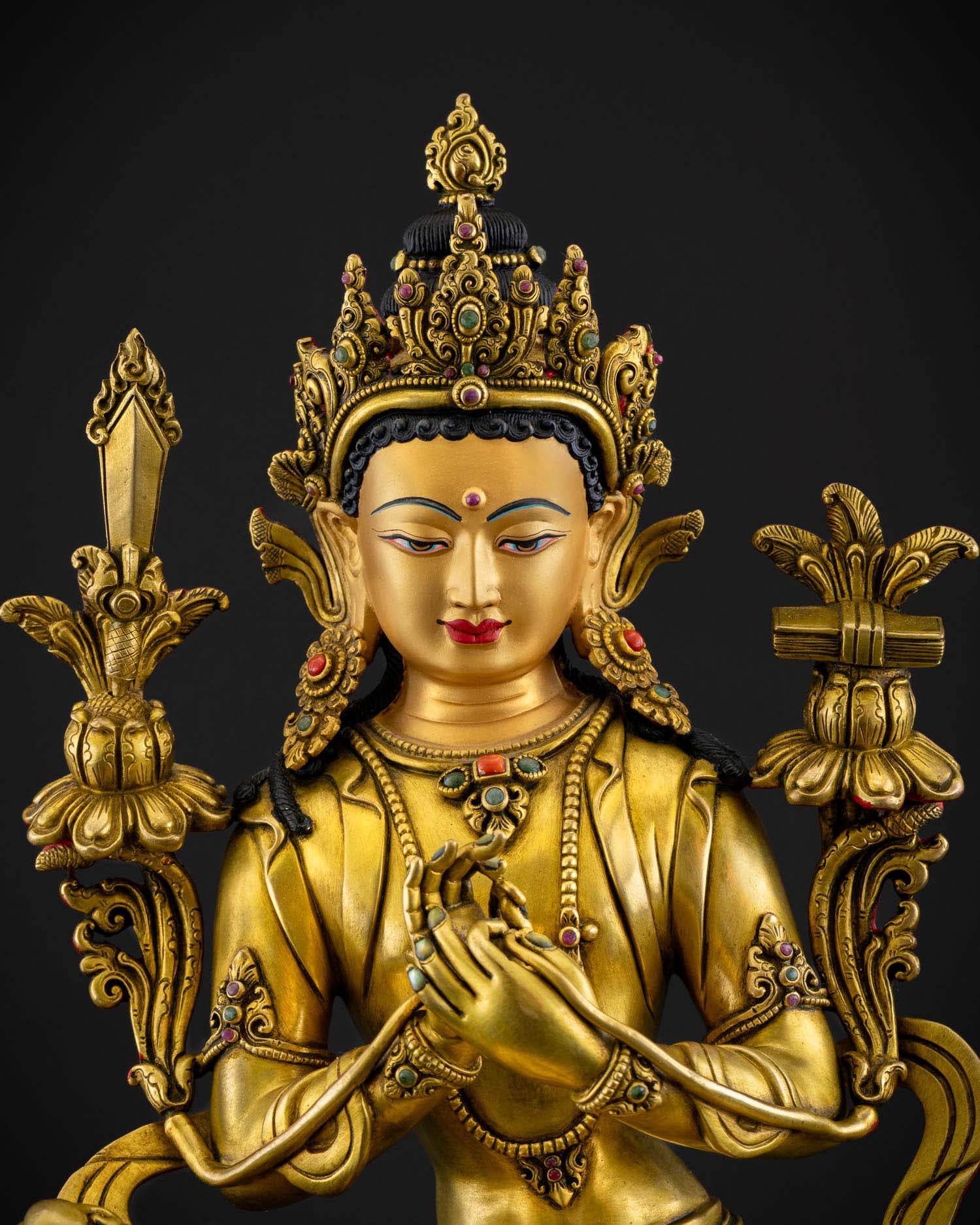 Close up detail of Manjushri face and jeweled crown showing serene expression gold fire gilded finish and intricate Newari craftsmanship