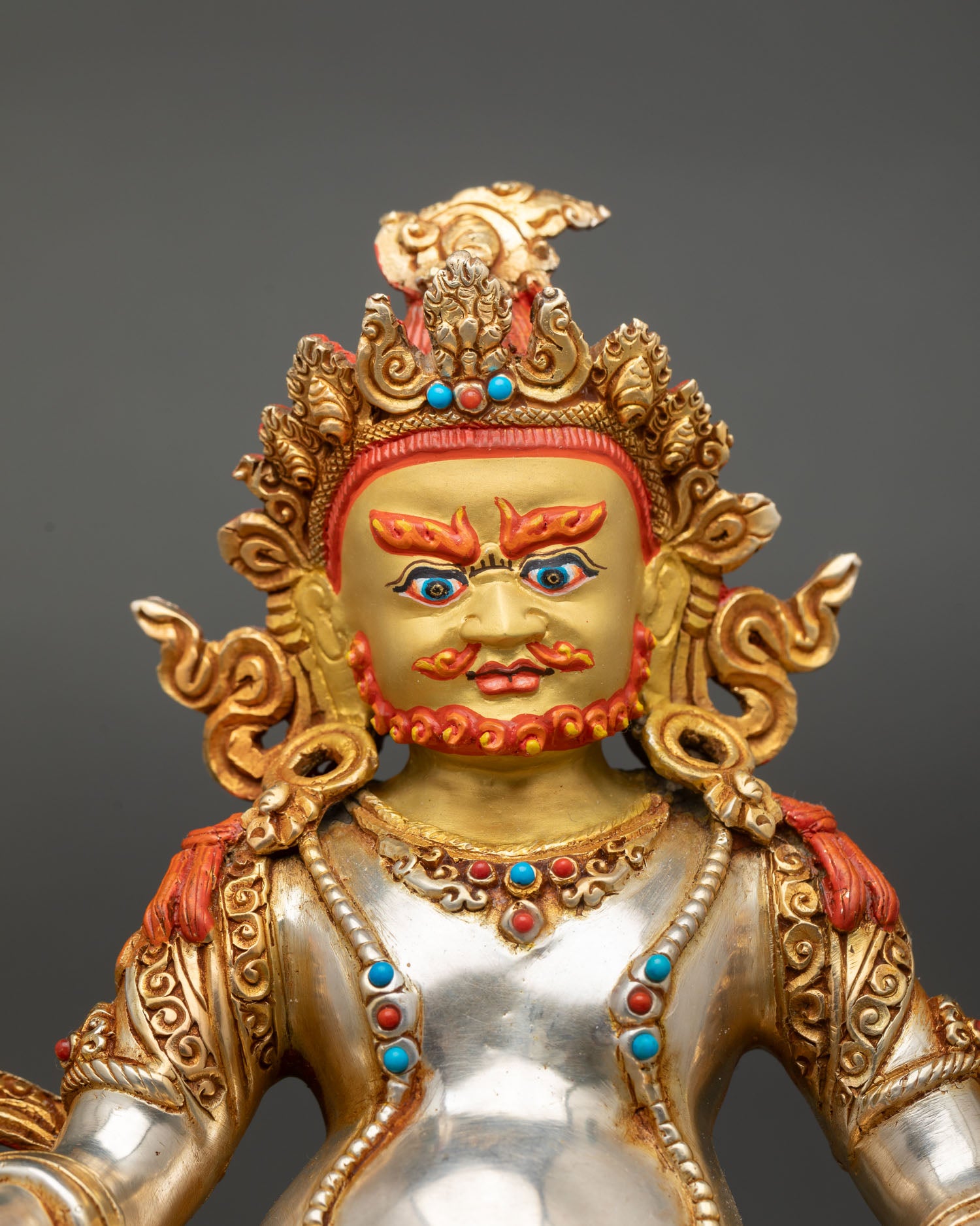 Close up Dzambhala face gold painted copper statue with silver plated details and semi precious stone inlay Buddhist art Nepal
