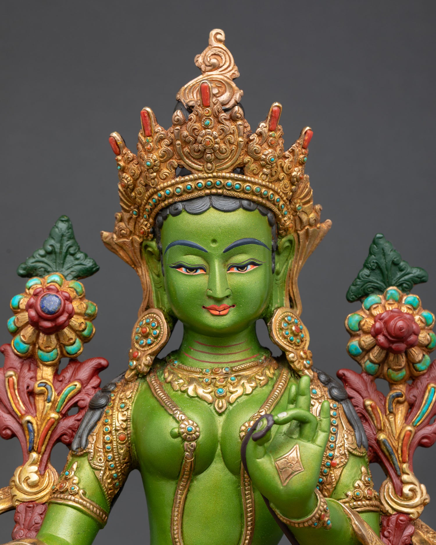 Close up Green Tara face with serene expression and intricate Himalayan Buddhist engraved metalwork