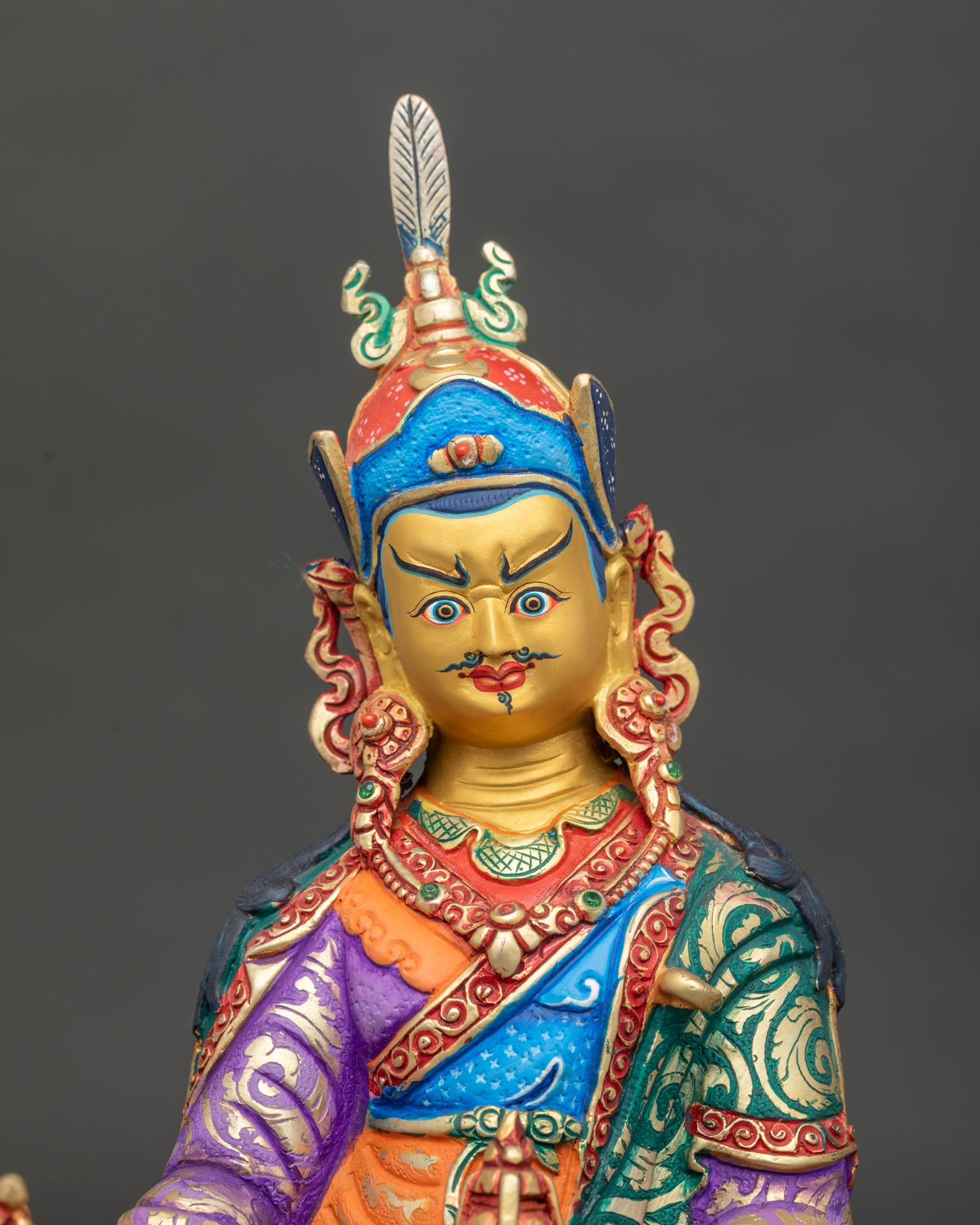 Close up Guru Rinpoche statue showing semi wrathful expression and intricate royal garment.