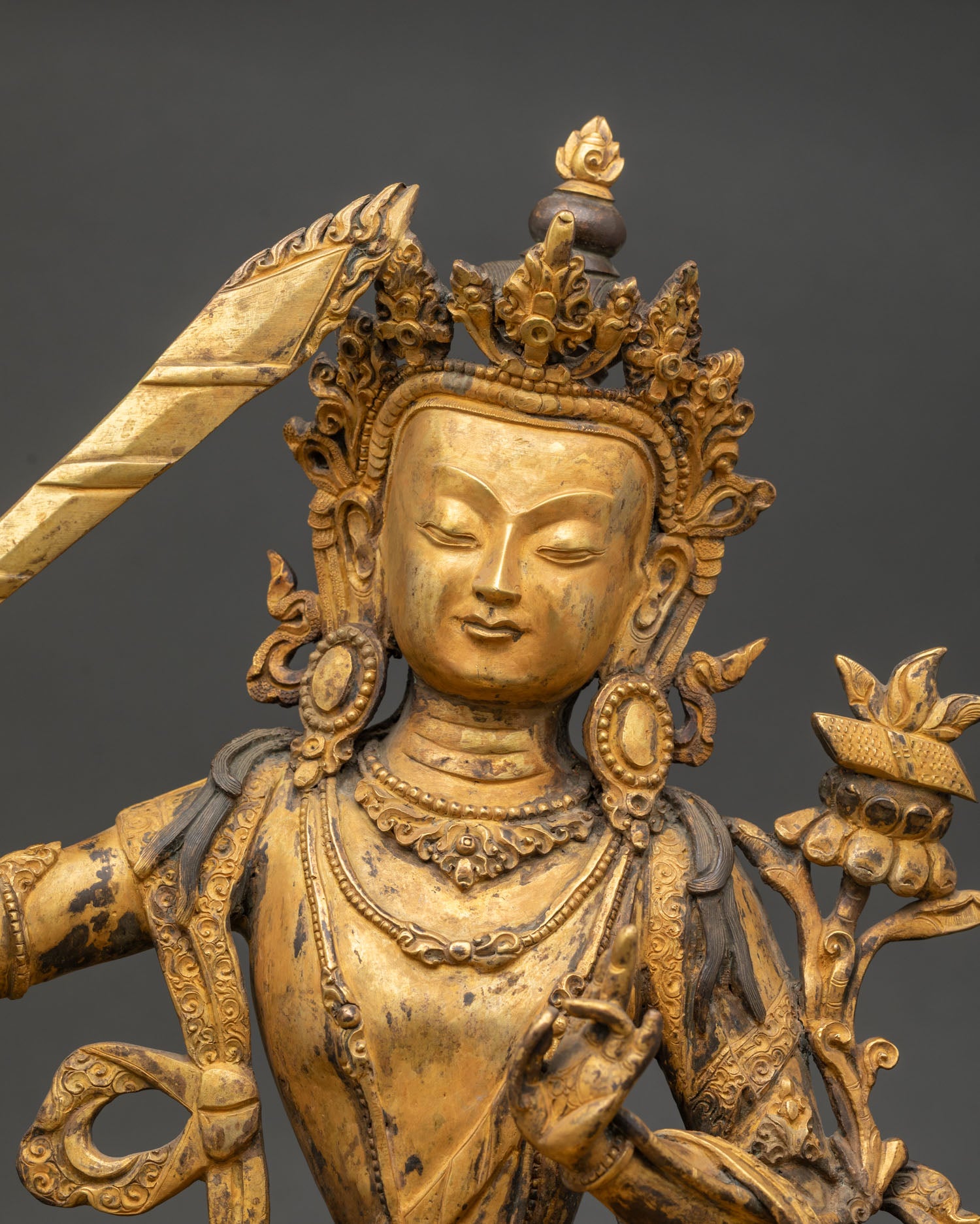 Close-up Manjushri Bodhisattva statue, detailed face, five jeweled crown, ornate jewelry, gold gilded finish, Himalayan Buddhist wisdom deity sculpture