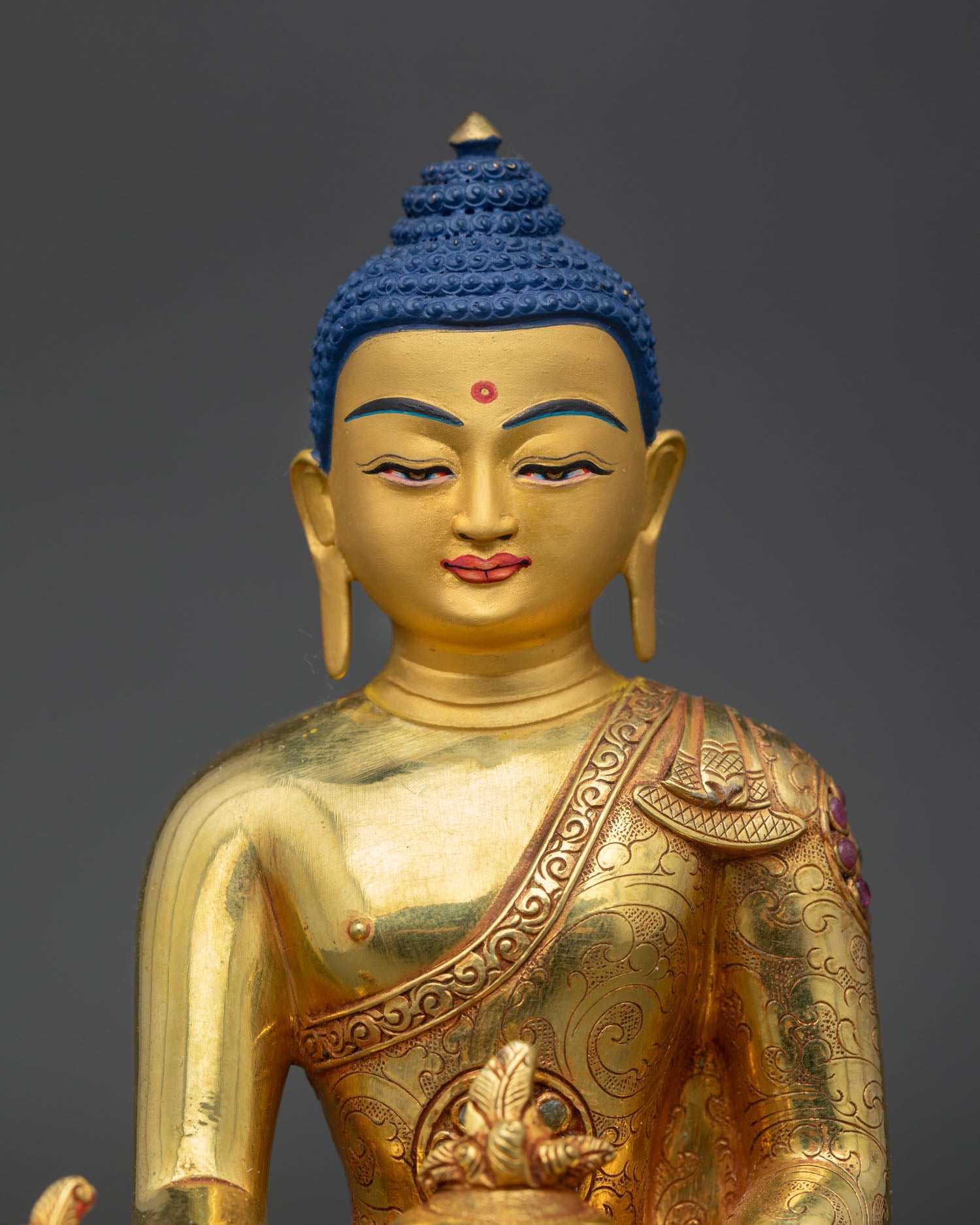 Close up Medicine Buddha sculpture showing gold painted face intricate monastic robes and traditional Newari craftsmanship from Patan, Nepal