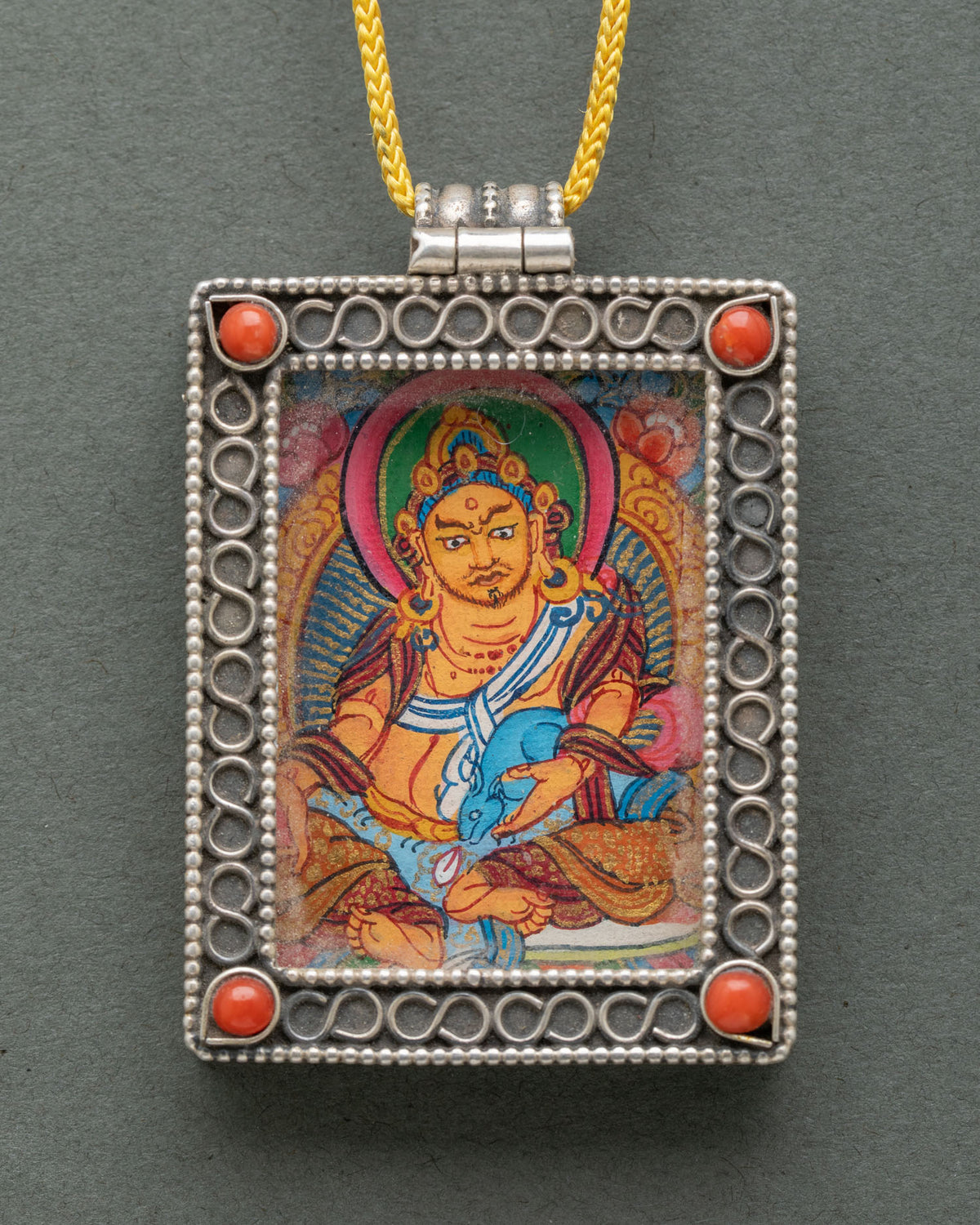 Close-up of a handcrafted Dzambhala locket showcasing delicate silver filigree, semi-precious coral stones, and traditional Newari craftsmanship from Nepal.