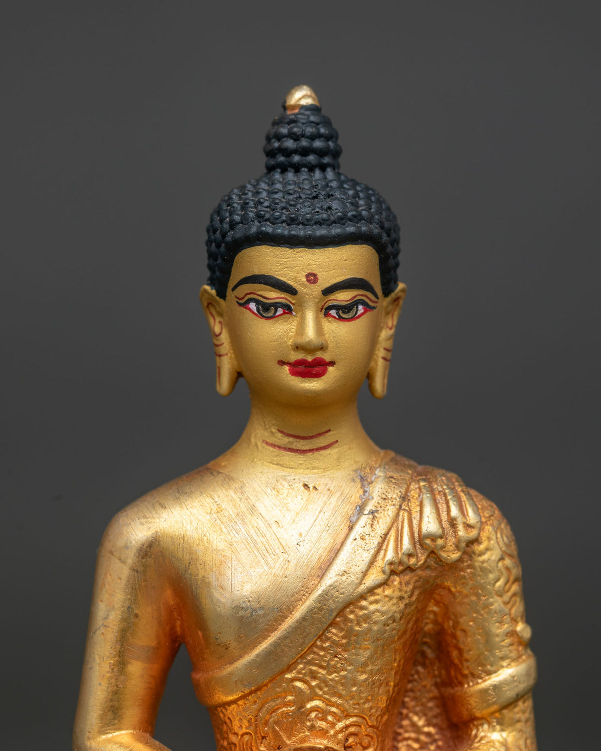 Close up of Amitabha Buddha statue showing gold painted face and serene expression in fine detail.
