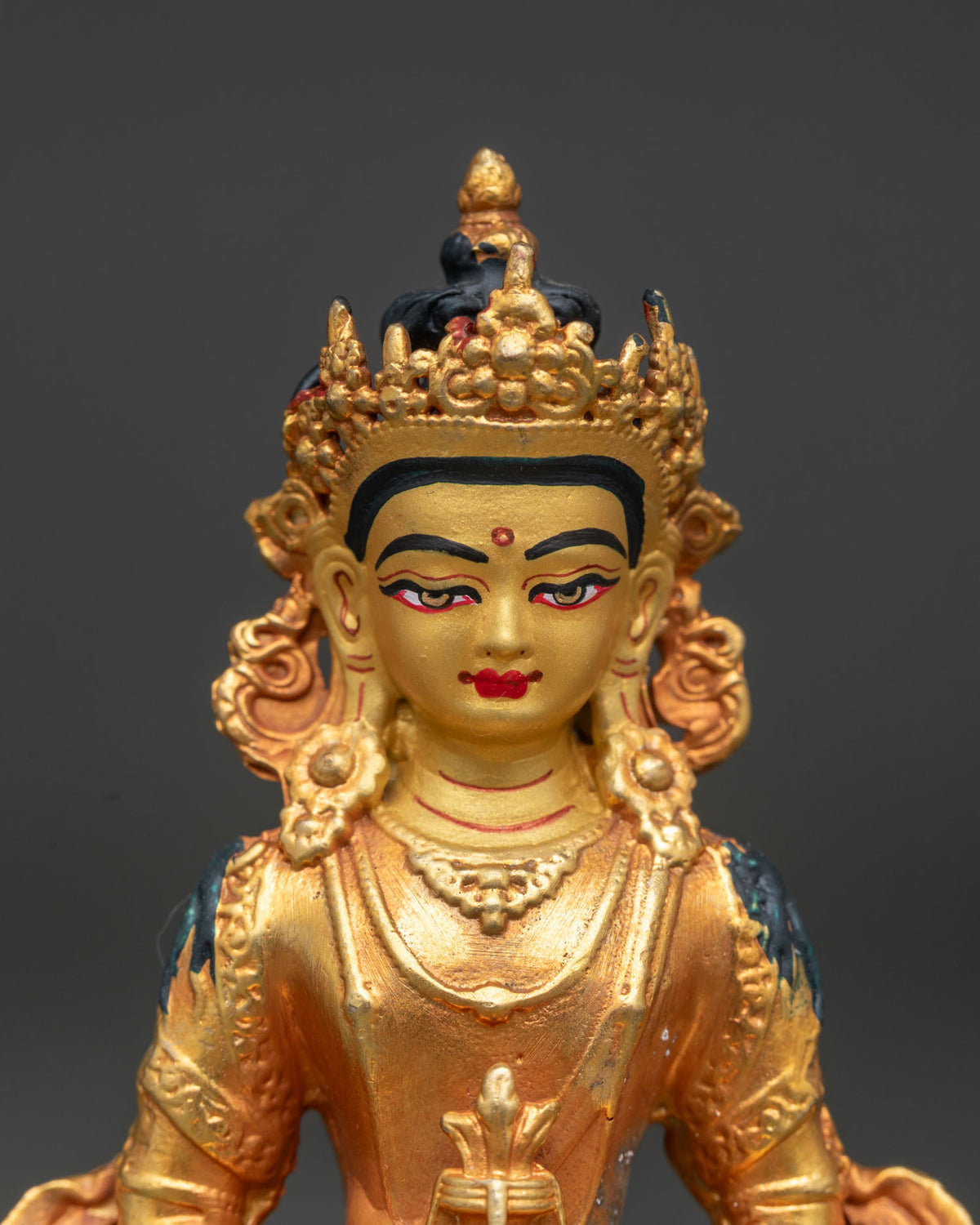 Close up of Amitayus Buddha statue with gold painted face and serene expression.