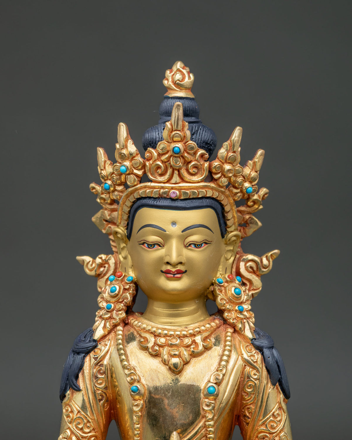 Close up of amitayus statue showing 24k gold painted face detailed crown and stone ornaments.