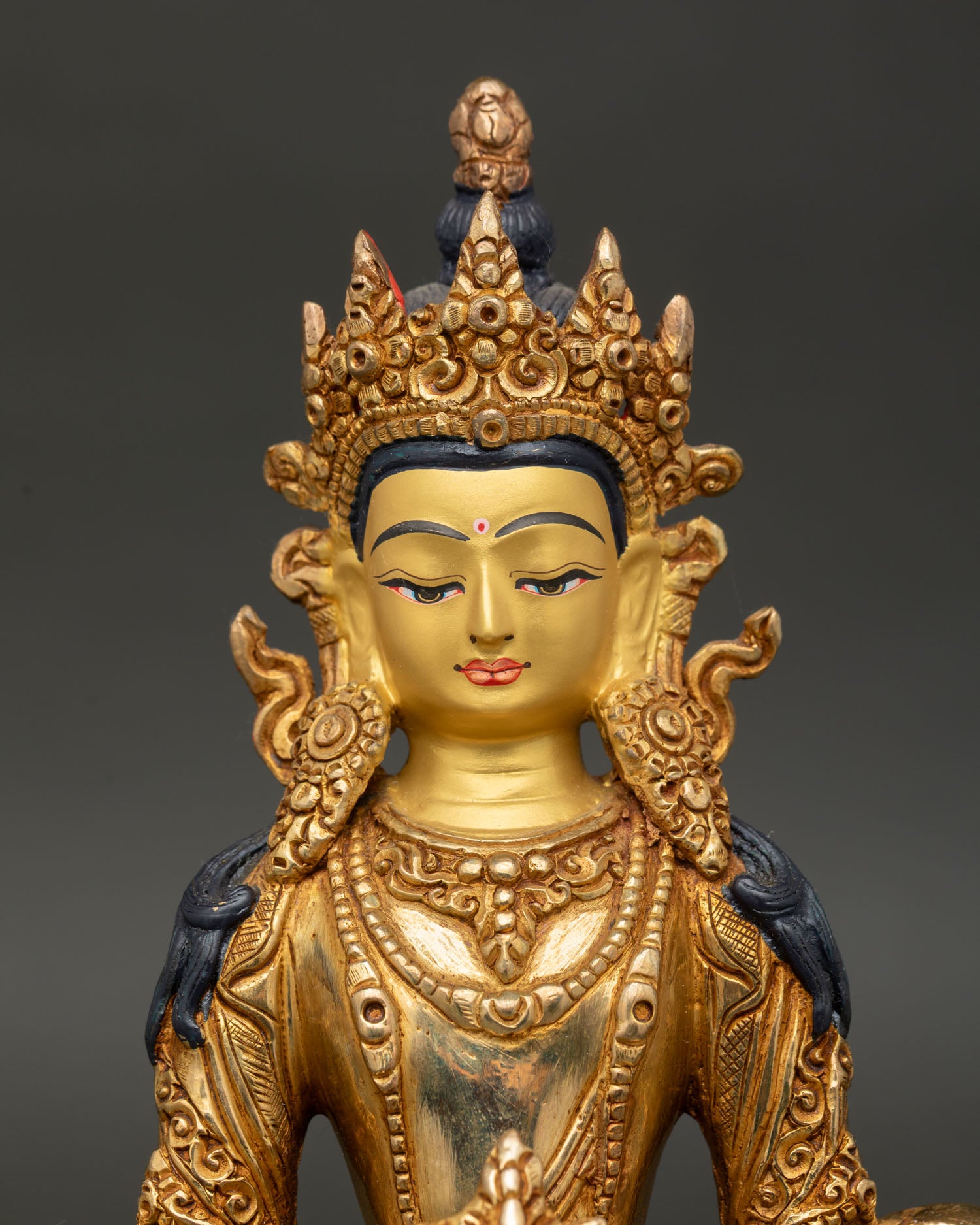 Close-up of Amitayus Statue with gold-painted face, serene expression and jeweled crown Nepal.