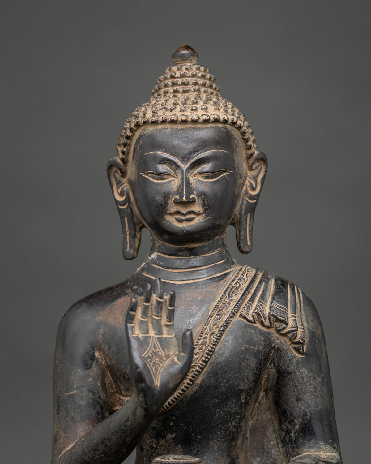 Close-up of Amoghasiddhi Buddha statue with serene face, curled hair and raised abhaya mudra hand