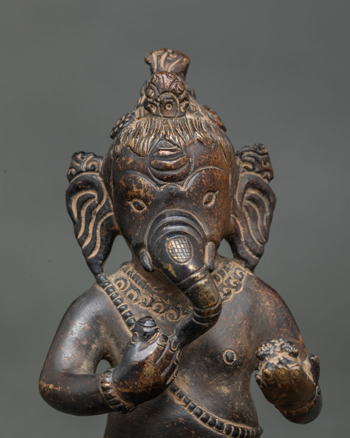 Close-up of Bal Ganesha face with long ears, curling trunk and detailed ornaments on copper statue