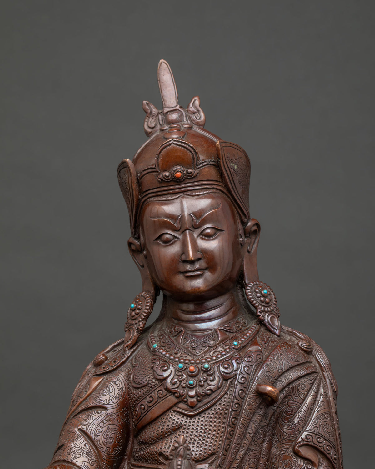 Close up of brown oxidized copper Guru Rinpoche statue with semi-precious stones and lotus pedestal
