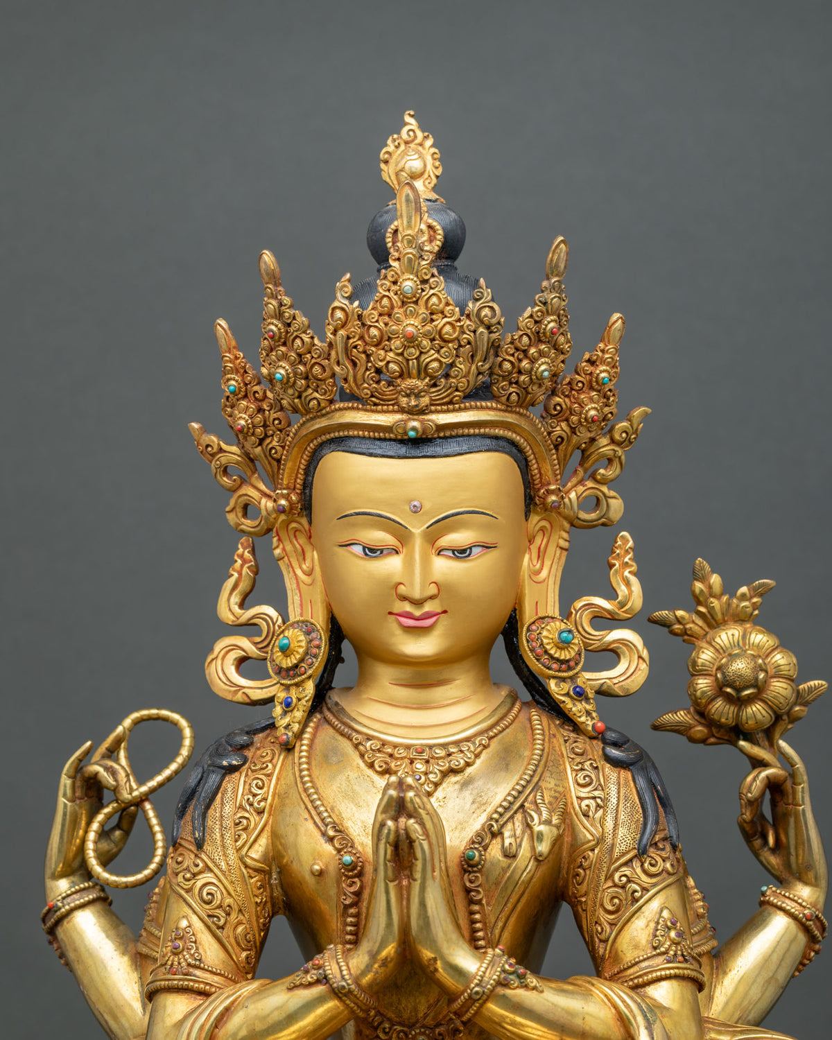 Close-up of Chenrezig statue face with jeweled five-point crown and hands in prayer gesture