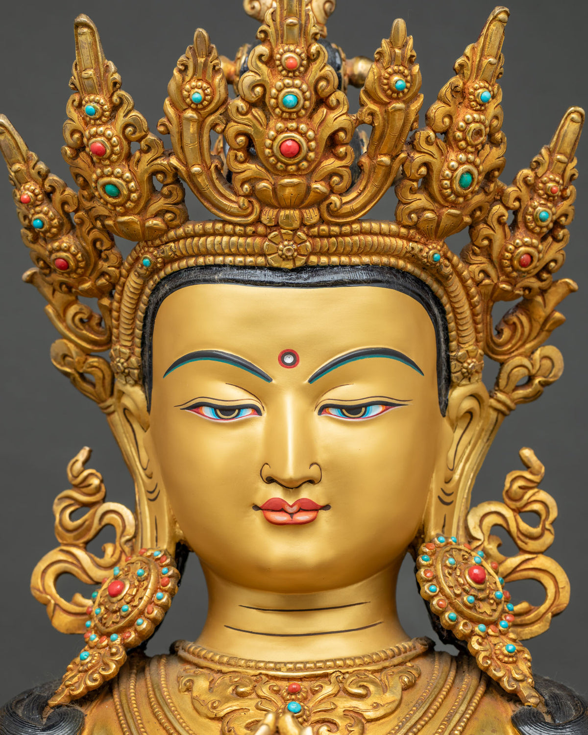 Close-up of Chenrezig statue face with turquoise and coral crown inlays, 24K gold finish