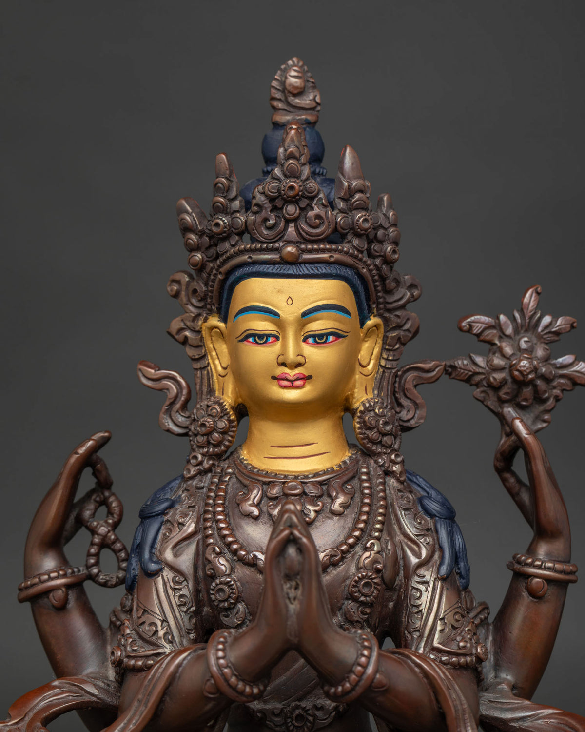 Close up of Chenrezig statue with 24k gold painted face and finely carved floral details.