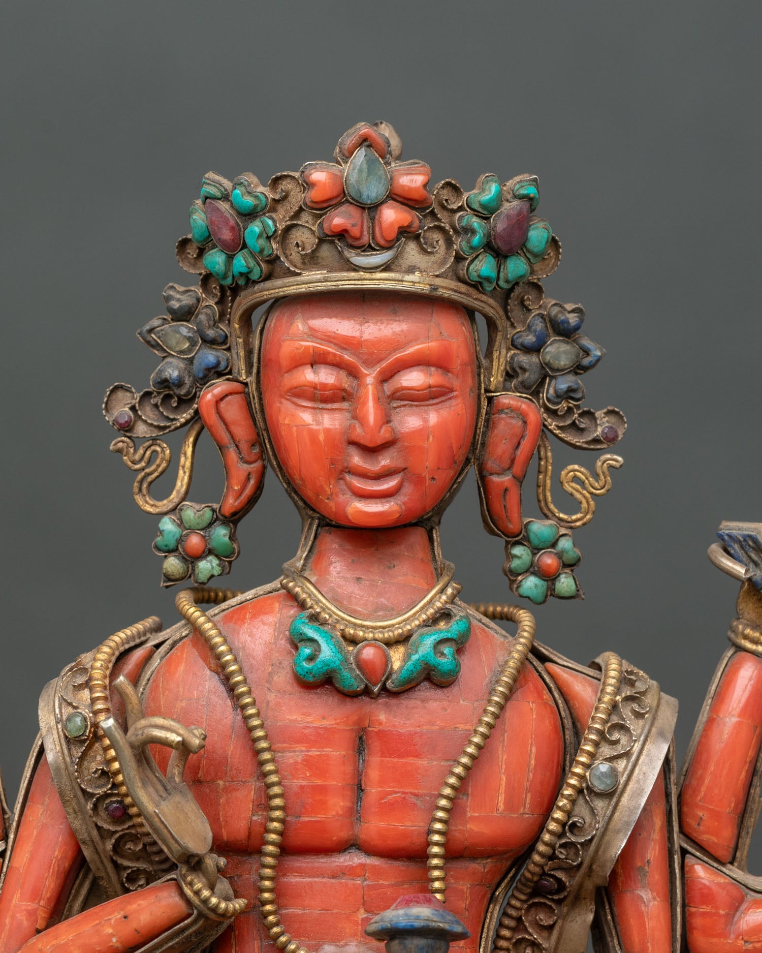 Close-up of coral Avalokiteshvara statue showing semi-precious stone inlay and gold-gilded details