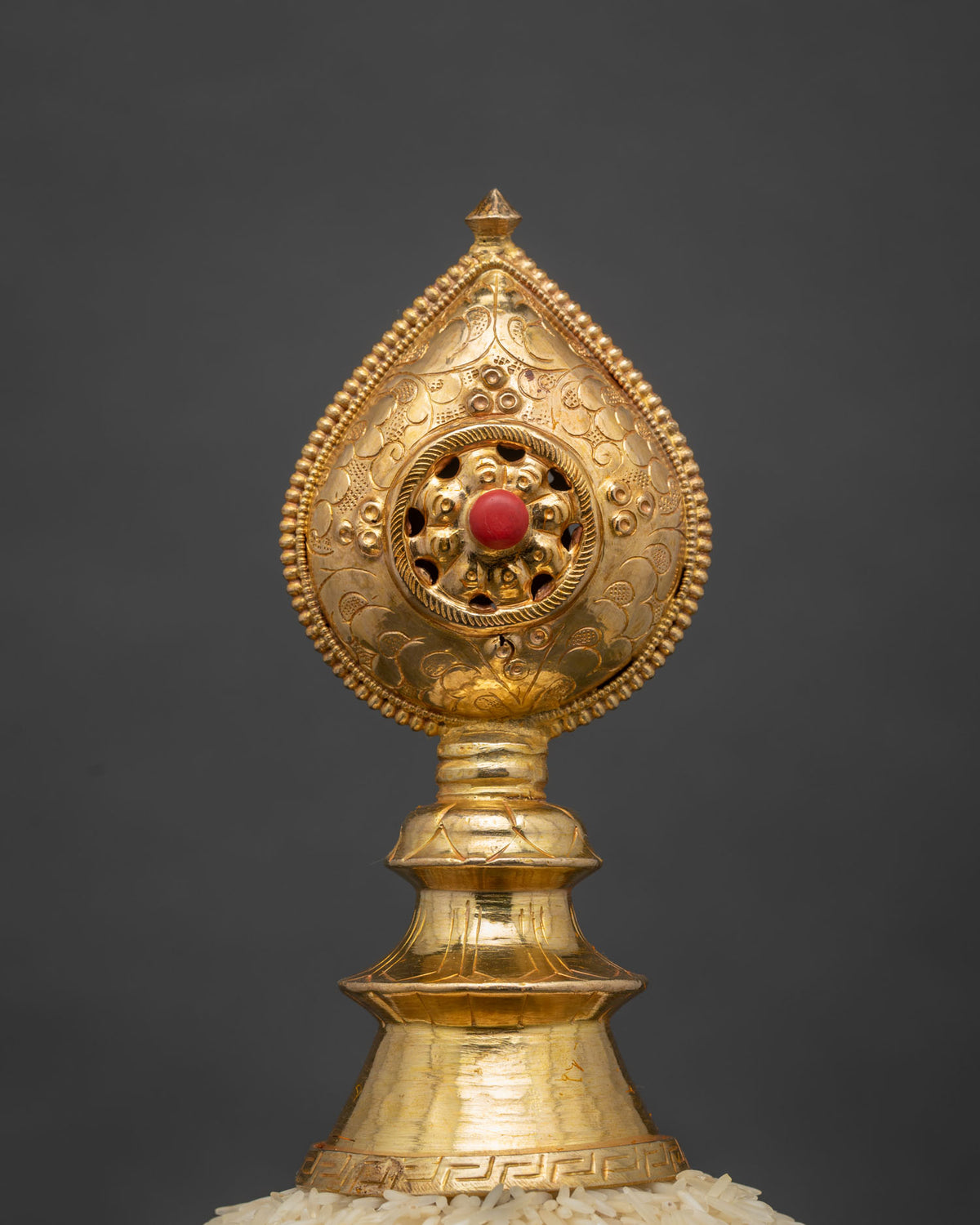 Close-up of coral jewel finial on gold Tibetan Mandala Offering Set