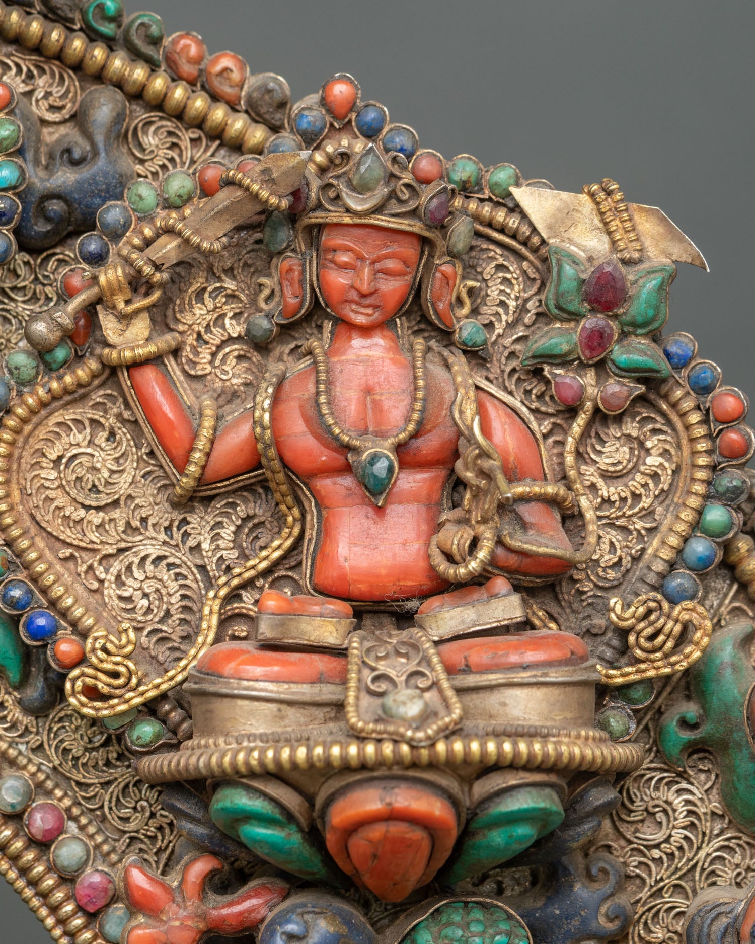 Close-up of coral Manjushri attendant holding wisdom sword, set in ornate gold aureole with gemstone inlay