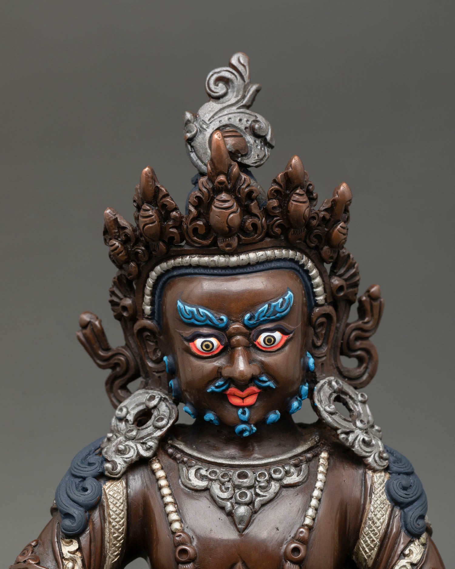 Close up of Dzambhala face with fierce compassionate expression in oxidized copper sculpture