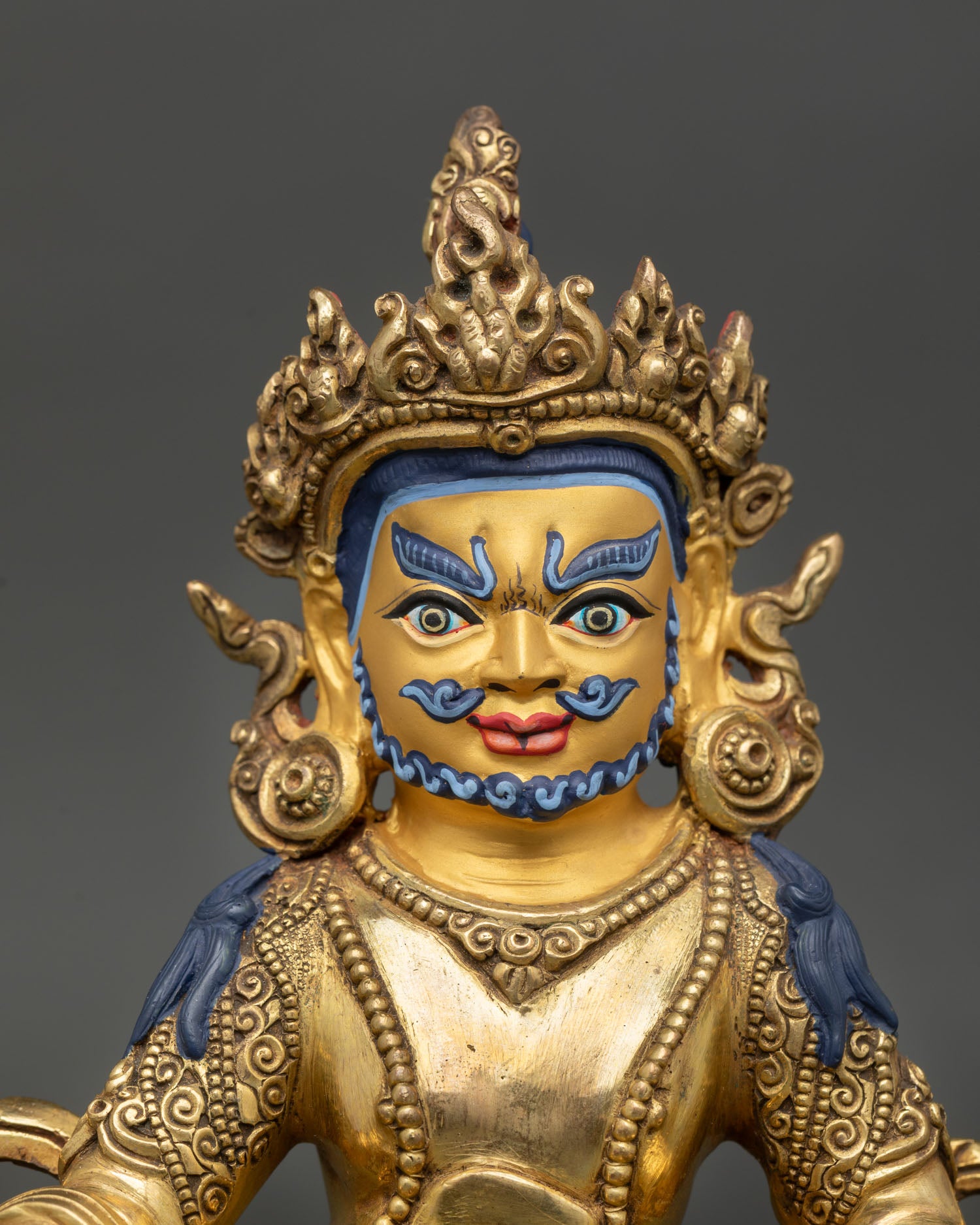 Close up of Dzambhala statue showing gold face, jeweled crown, and detailed craftsmanship from Nepal.