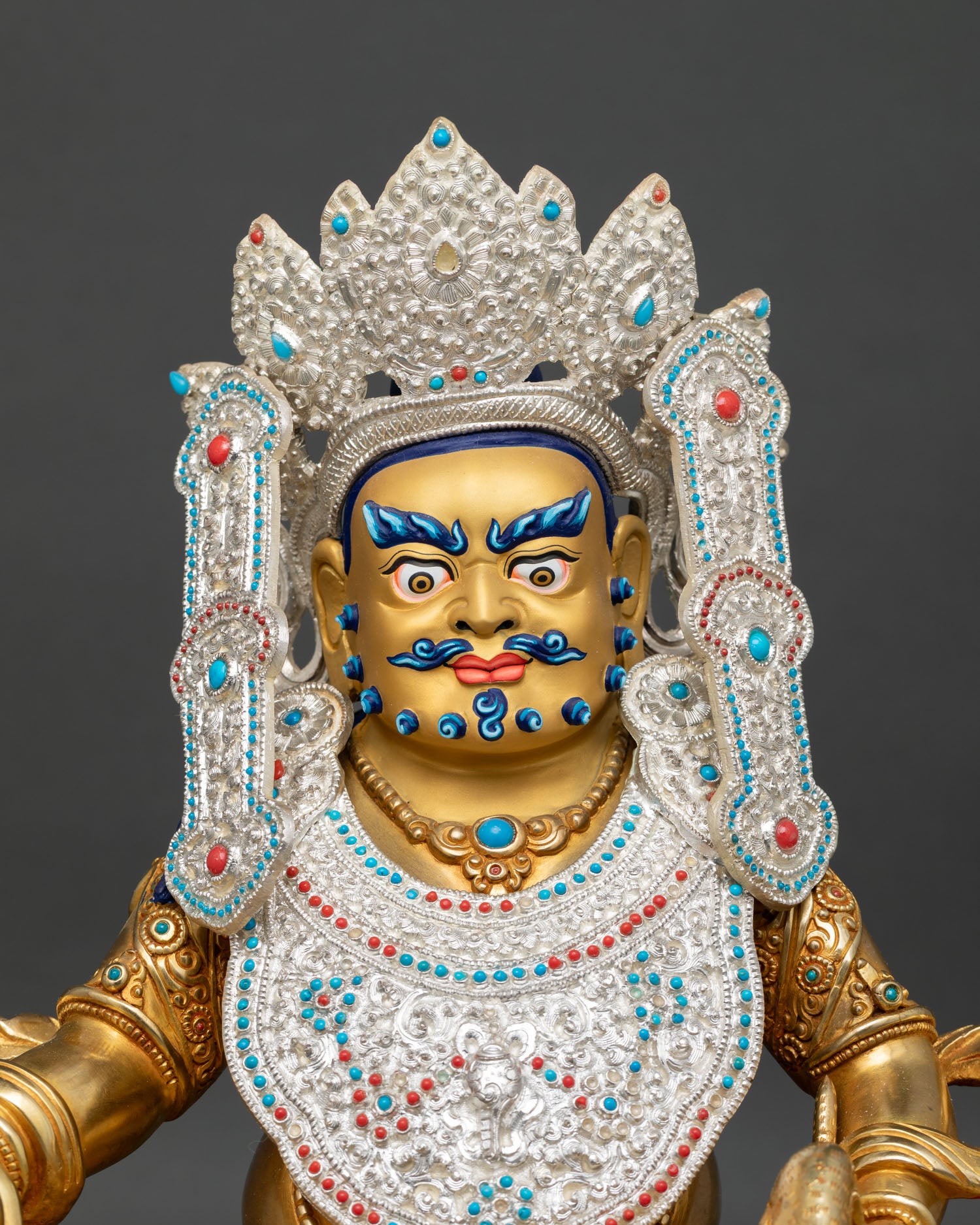 Close up of Dzambhala Statue showing jeweled crown, ornate ornaments, gold gilded details, and sacred facial expression