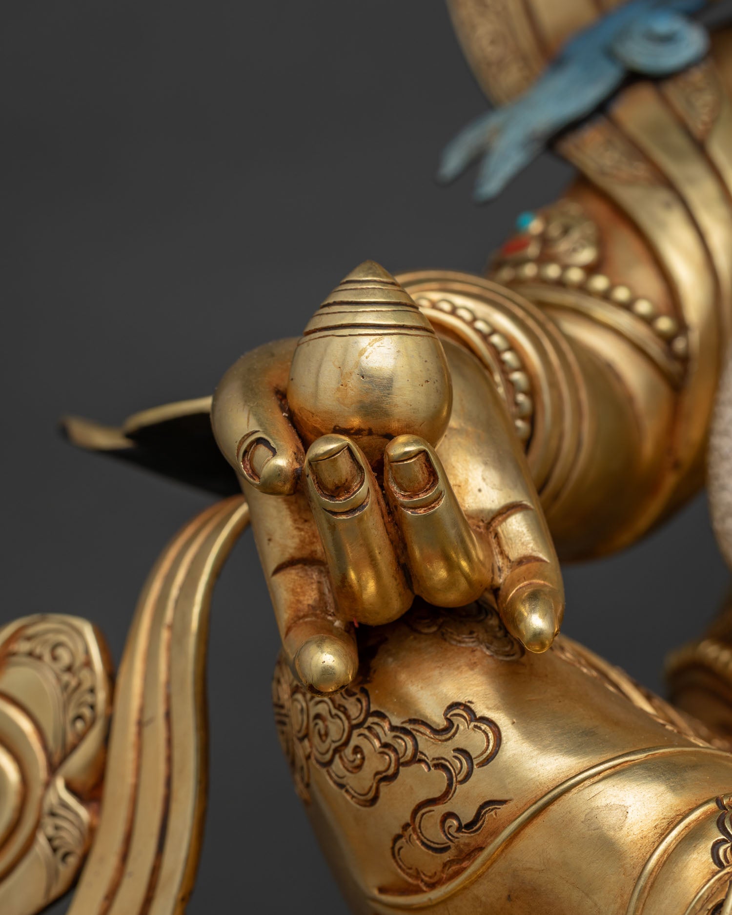 Close-up of Dzambhala's hand holding citron fruit with silk khata scarf