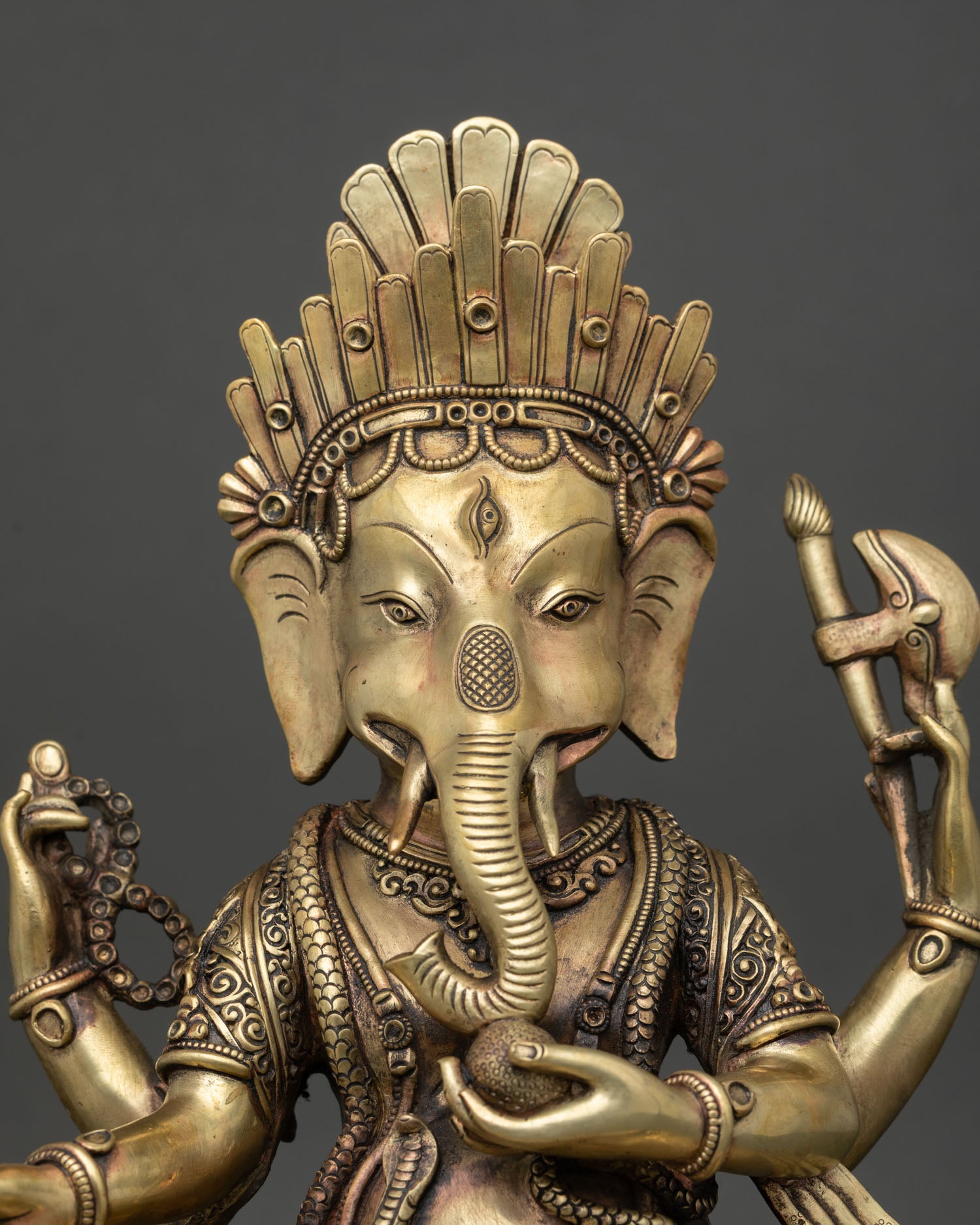 Close up of four-armed copper Ganesh idol holding traditional attributes on lotus throne.