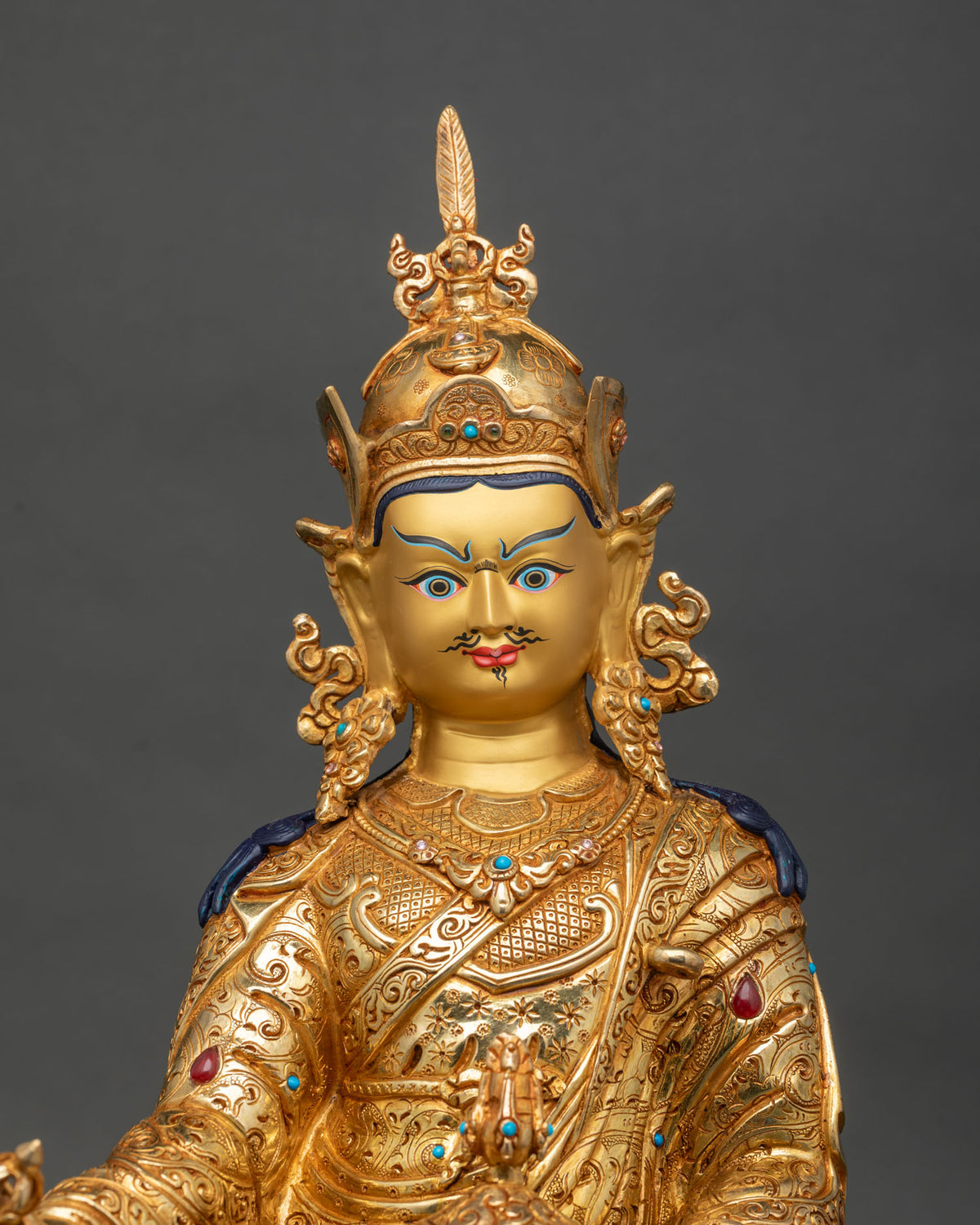 Close up of gold gilded Guru Rinpoche statue with vajra, kapala and engraved robe