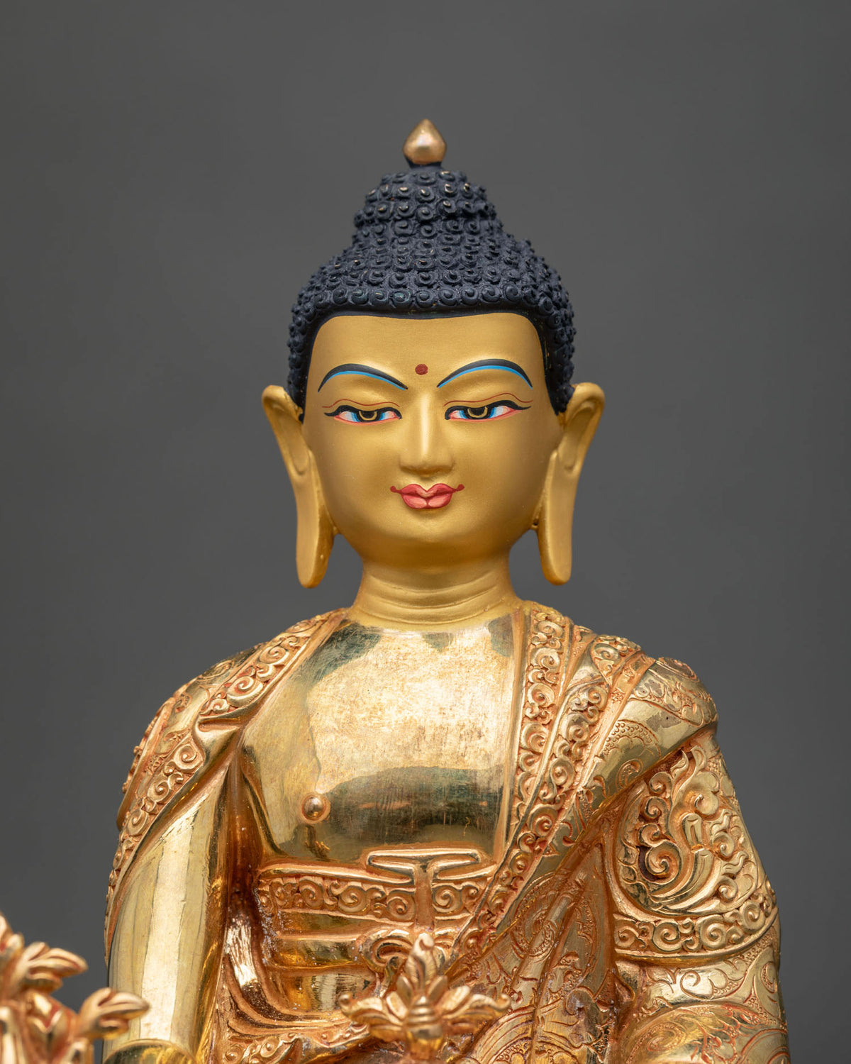 Close-up of gold Medicine Buddha face with blue brows, red bindu, and dark curled hair