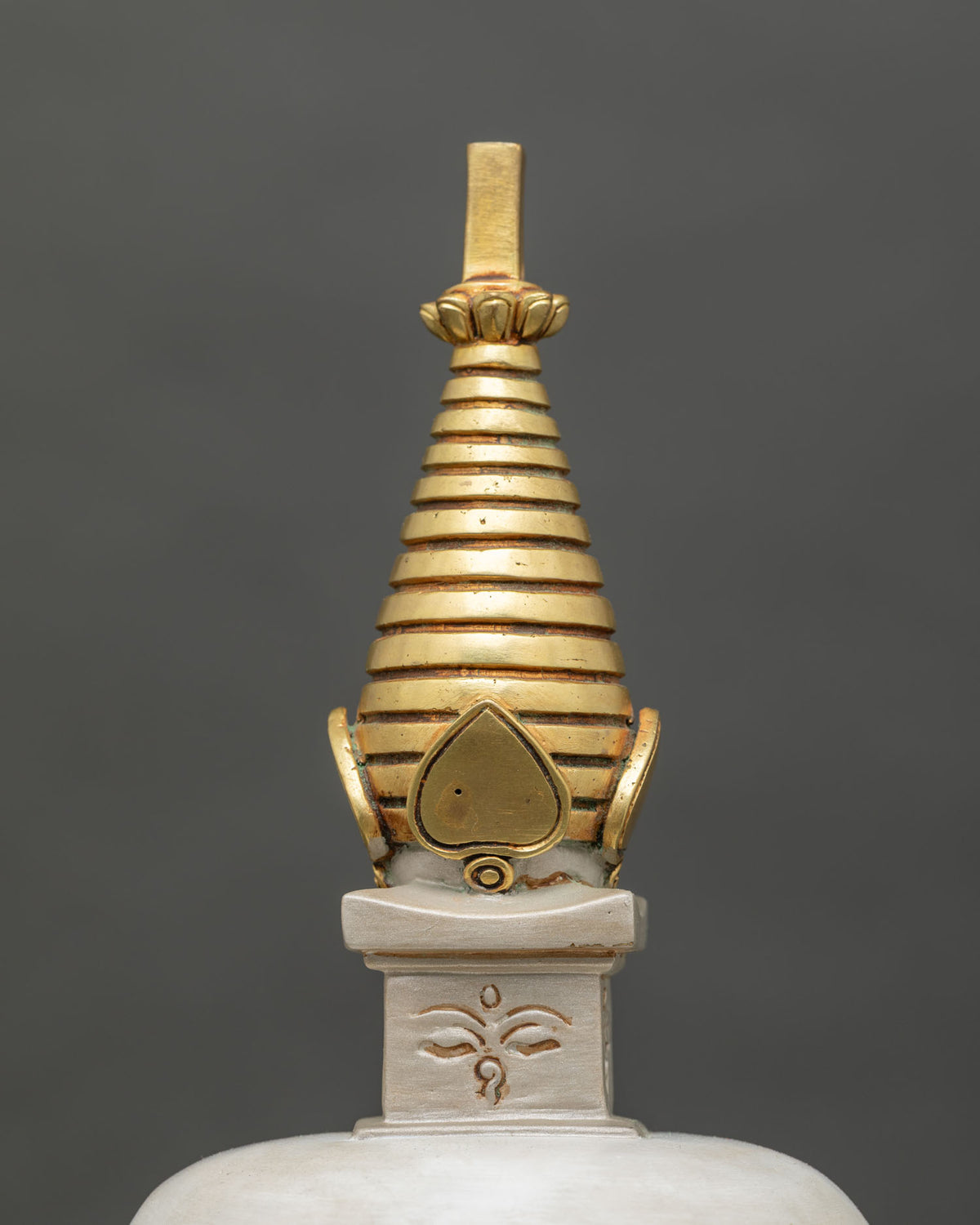 Close-up of golden tiered spire and carved Buddha eyes on the harmika of a copper Buddhist stupa